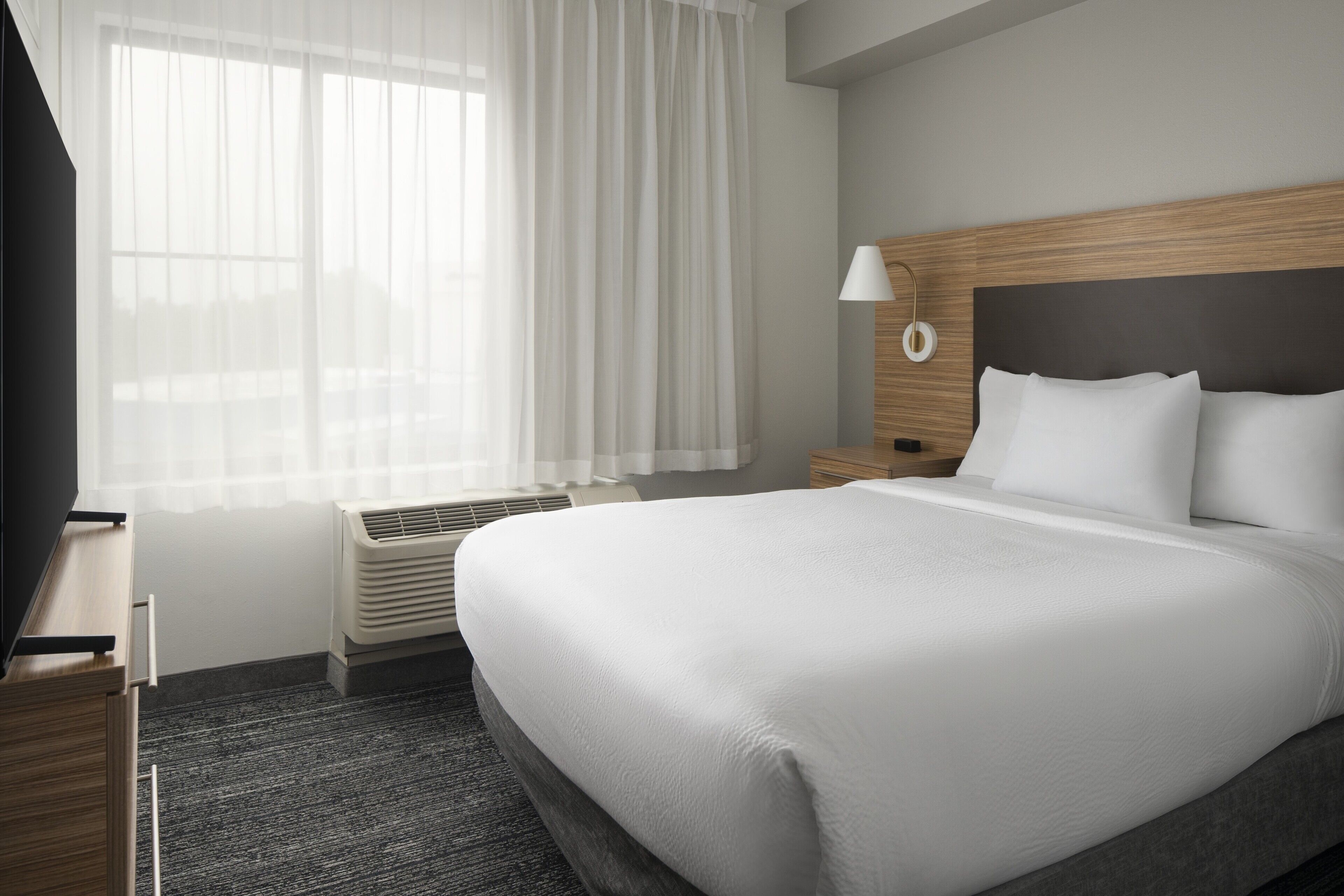 Una habitación de hotel con una cama grande, una mesita de noche, una lámpara y una ventana con cortinas.