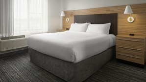 Habitación de hotel moderna con una cama grande, cabecera de madera, dos mesitas de noche con lámparas, una ventana con cortinas translúcidas y un equipo de aire acondicionado integrado.