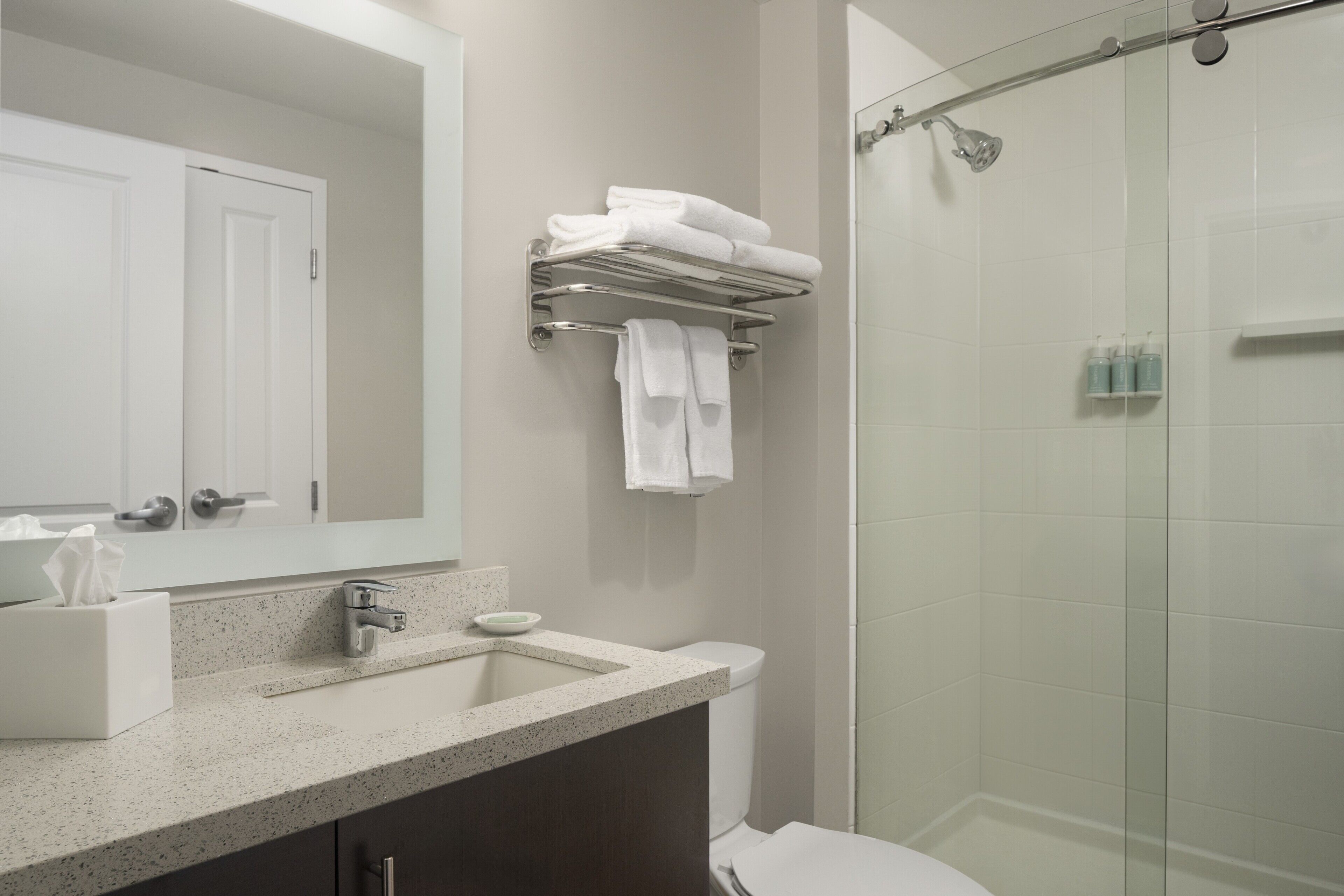 A modern bathroom with a large mirror, a sink with a soap dish, a towel rack, and a glass shower enclosure.