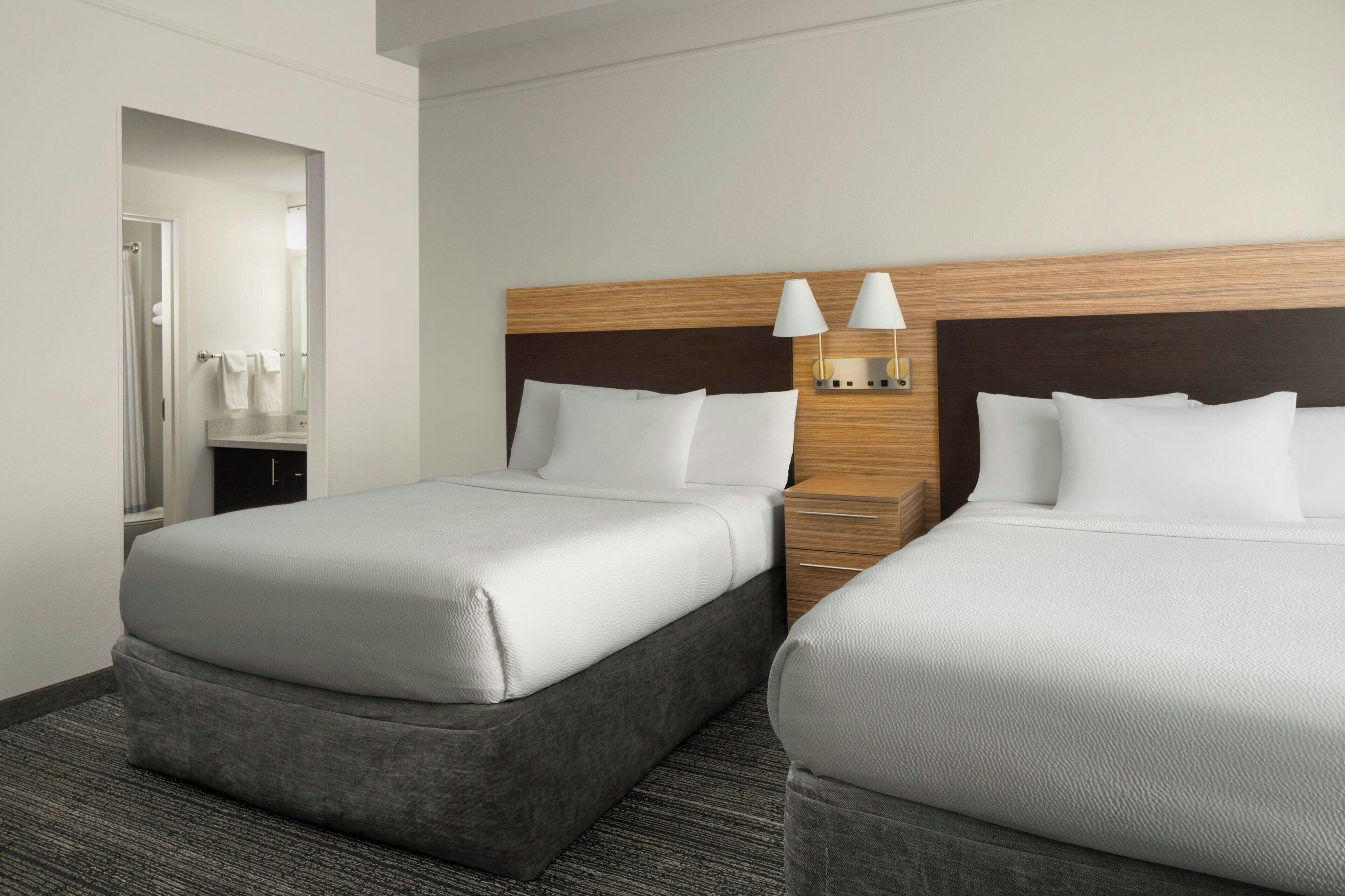 A hotel room with two beds, a wooden headboard, a nightstand, and a mirror.