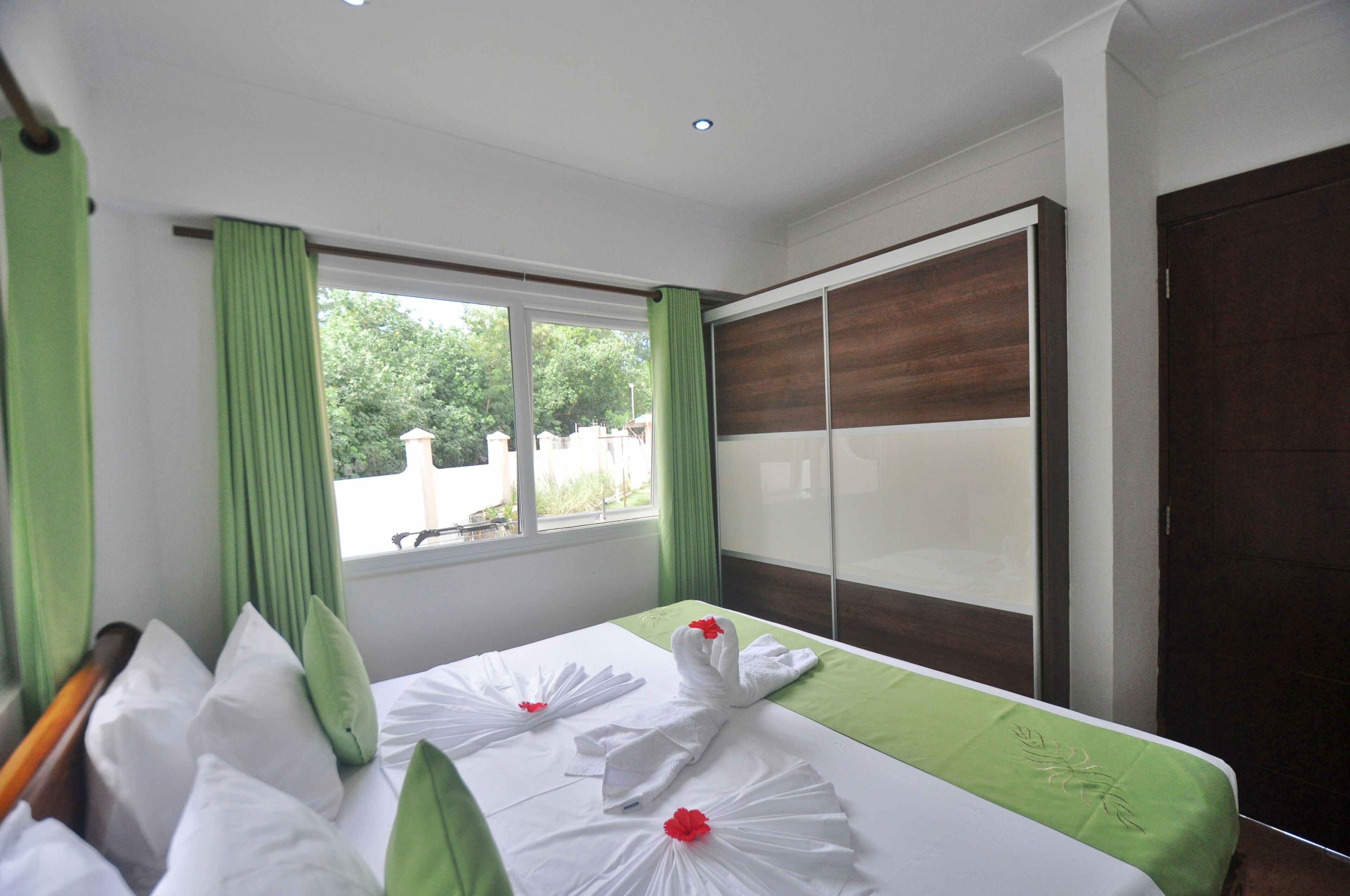 A hotel room with a bed, green curtains, a window with a view, and a wardrobe.