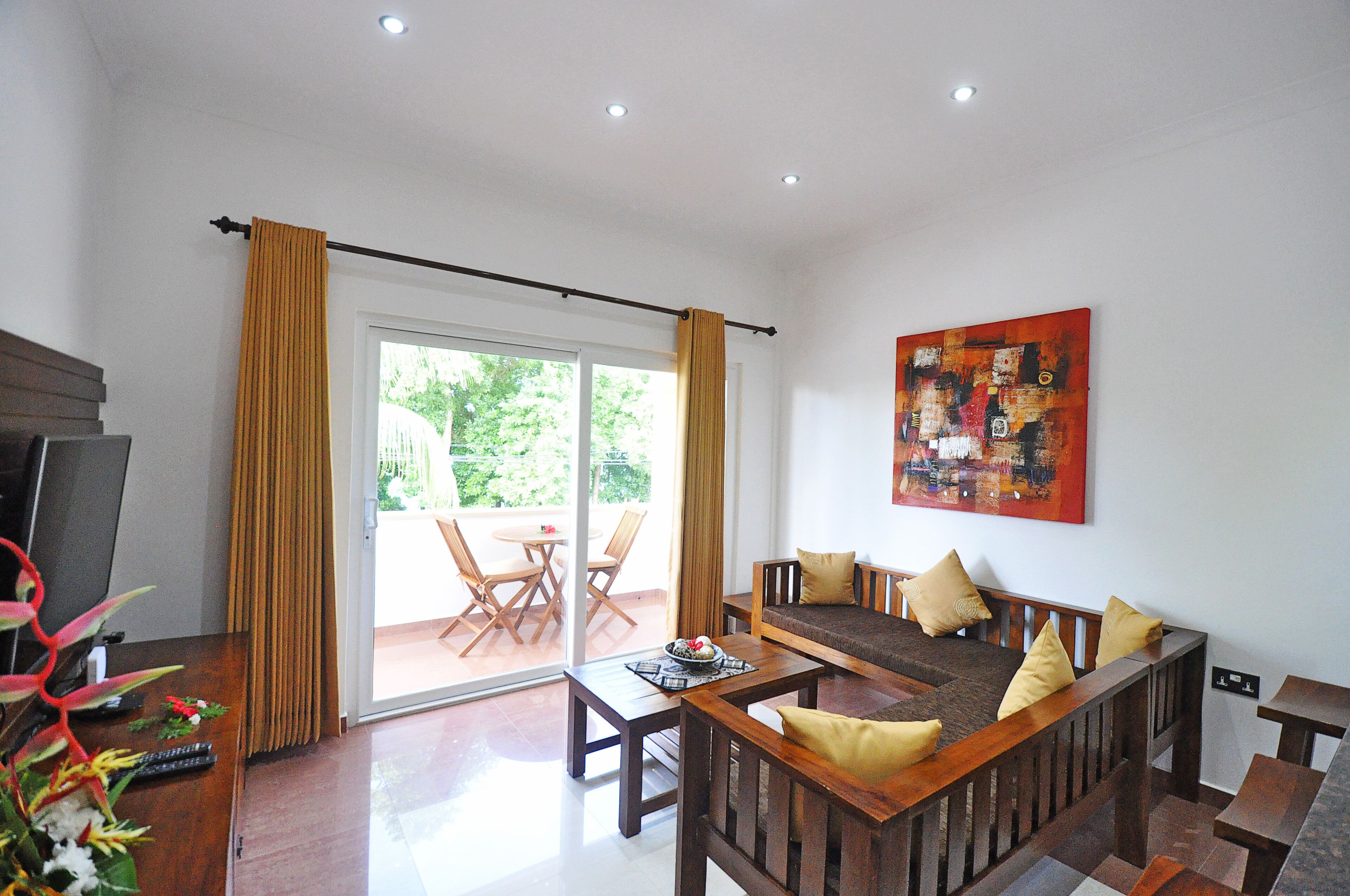 A living room with a sofa, coffee table, and a TV. There is a sliding glass door leading to an outdoor area with a table and chairs.
