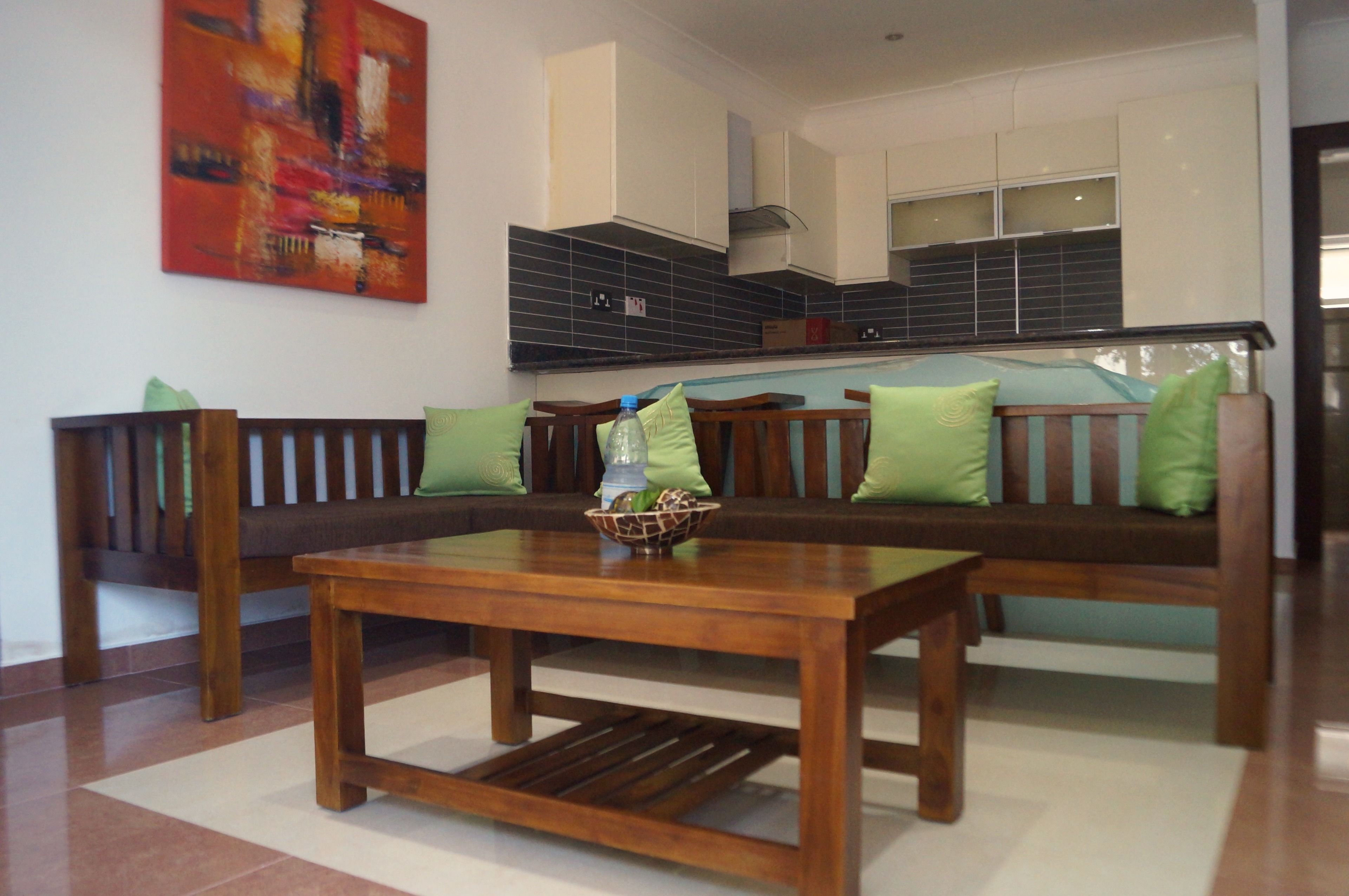 A living room with a wooden bench, a coffee table, and a kitchen in the background.