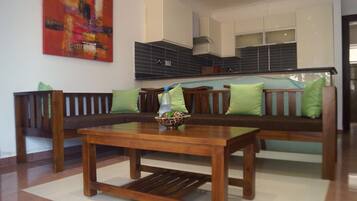 A living room with a wooden bench, a coffee table, and a kitchen in the background.