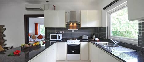 A modern kitchen with white cabinets, a stove, a microwave, and a sink.