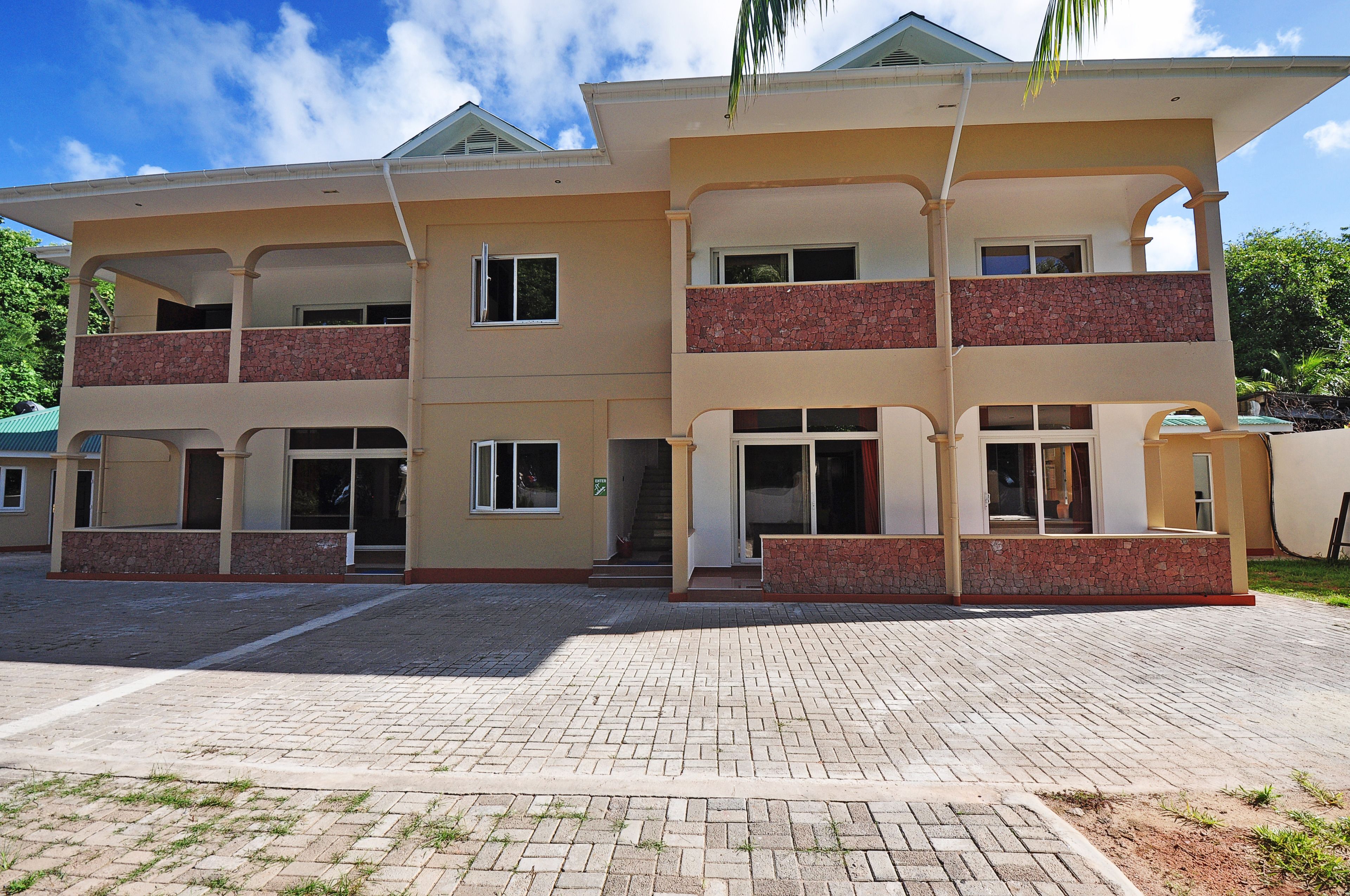 A multi-story building with a flat roof, balconies, and a paved entrance area.