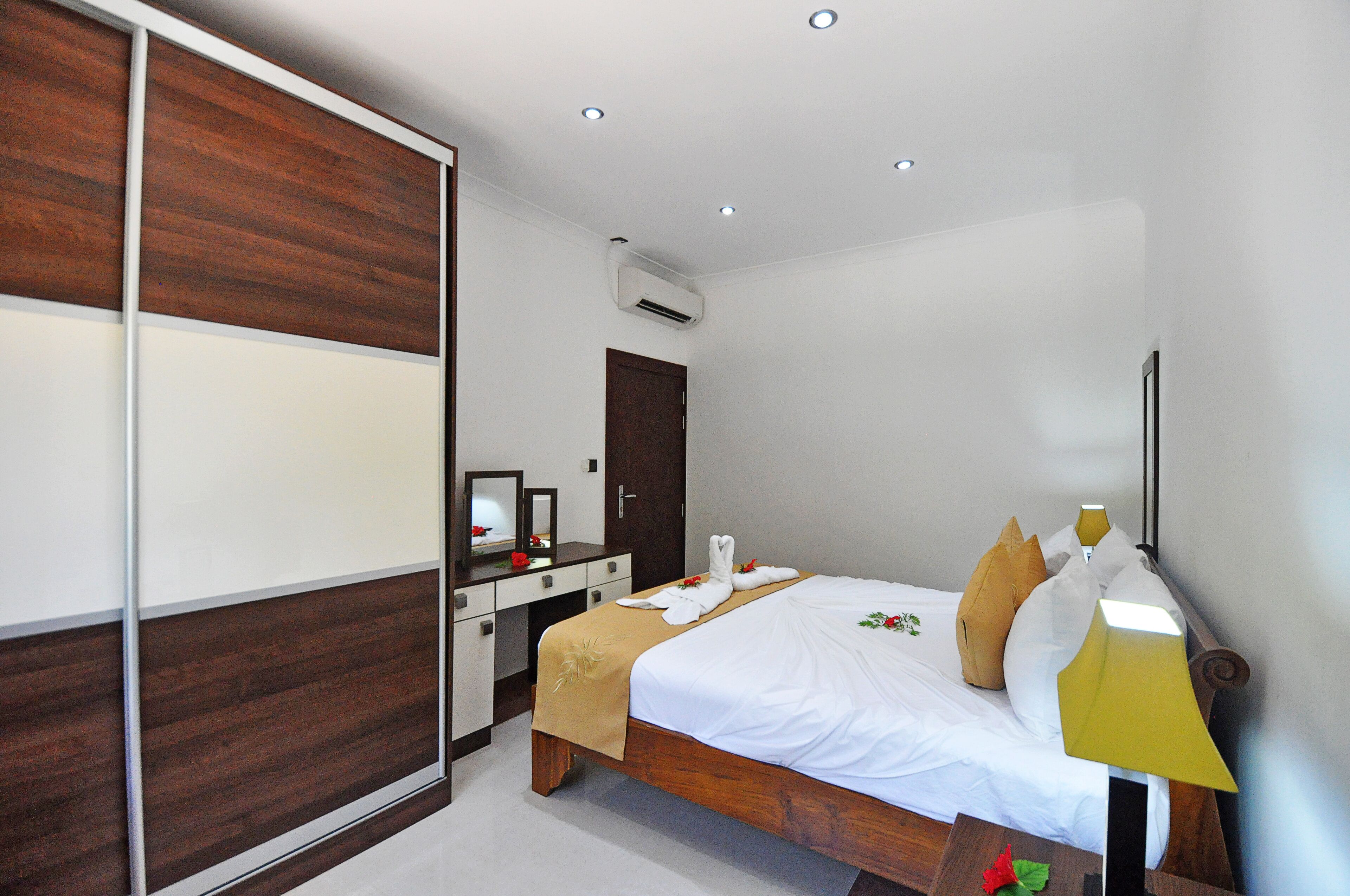 A hotel room with a wooden bed, a bedside table, a mirror, and a wardrobe.