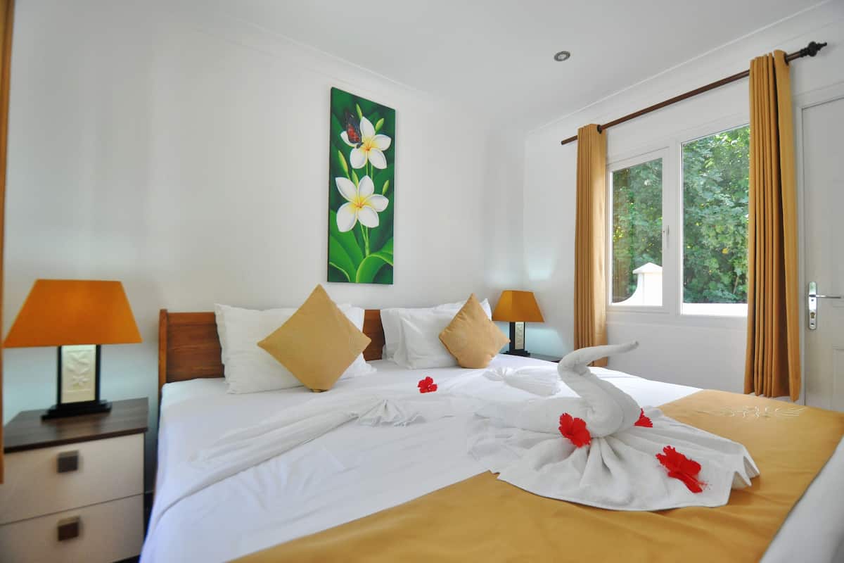 Ein Hotelzimmer mit einem aufgeräumten Bett, einem floralen Bild an der Wand und einem Fenster mit Vorhängen.
