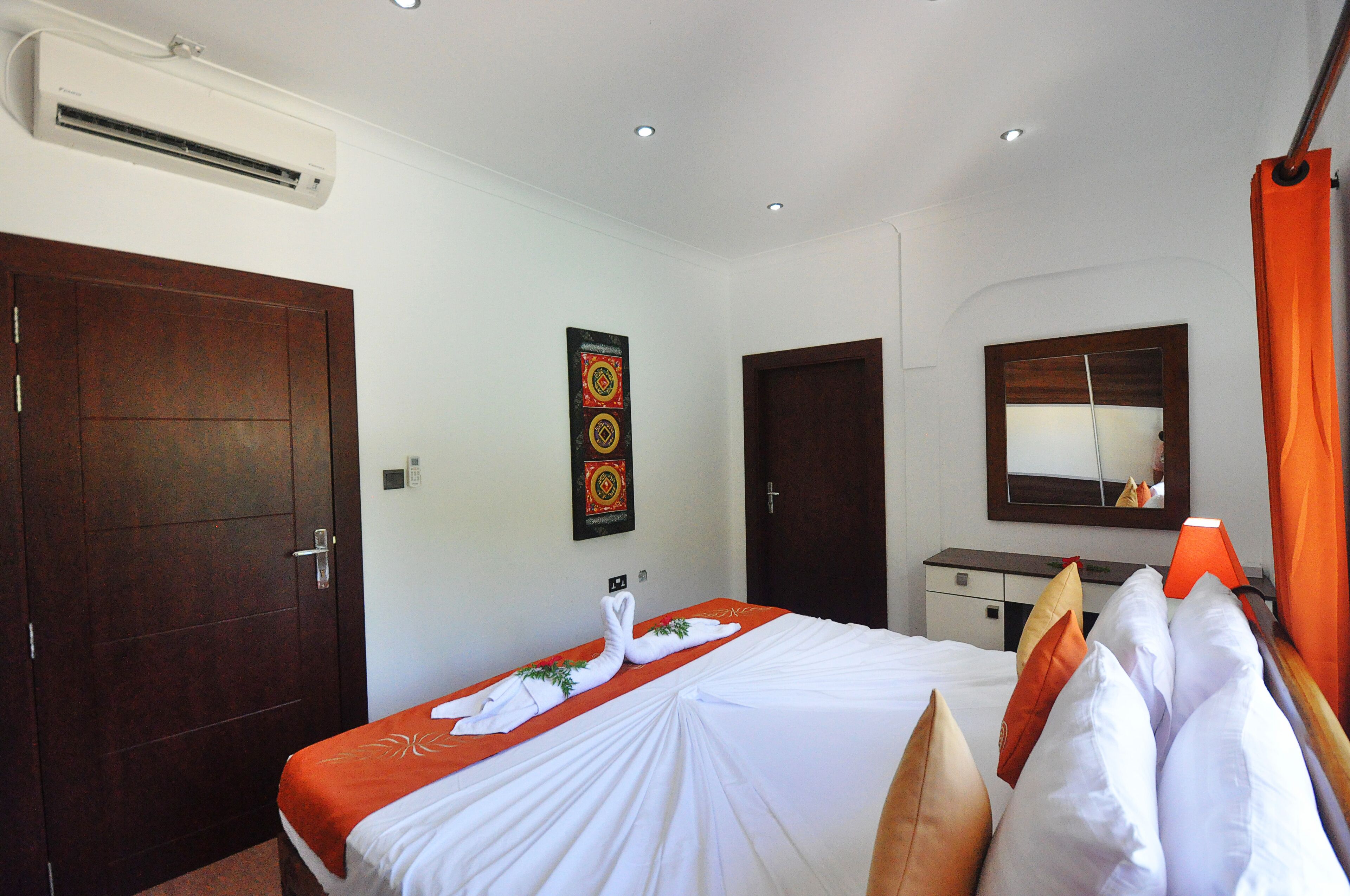 A hotel room with a large bed, a wooden wardrobe, a desk, and an air conditioning unit.