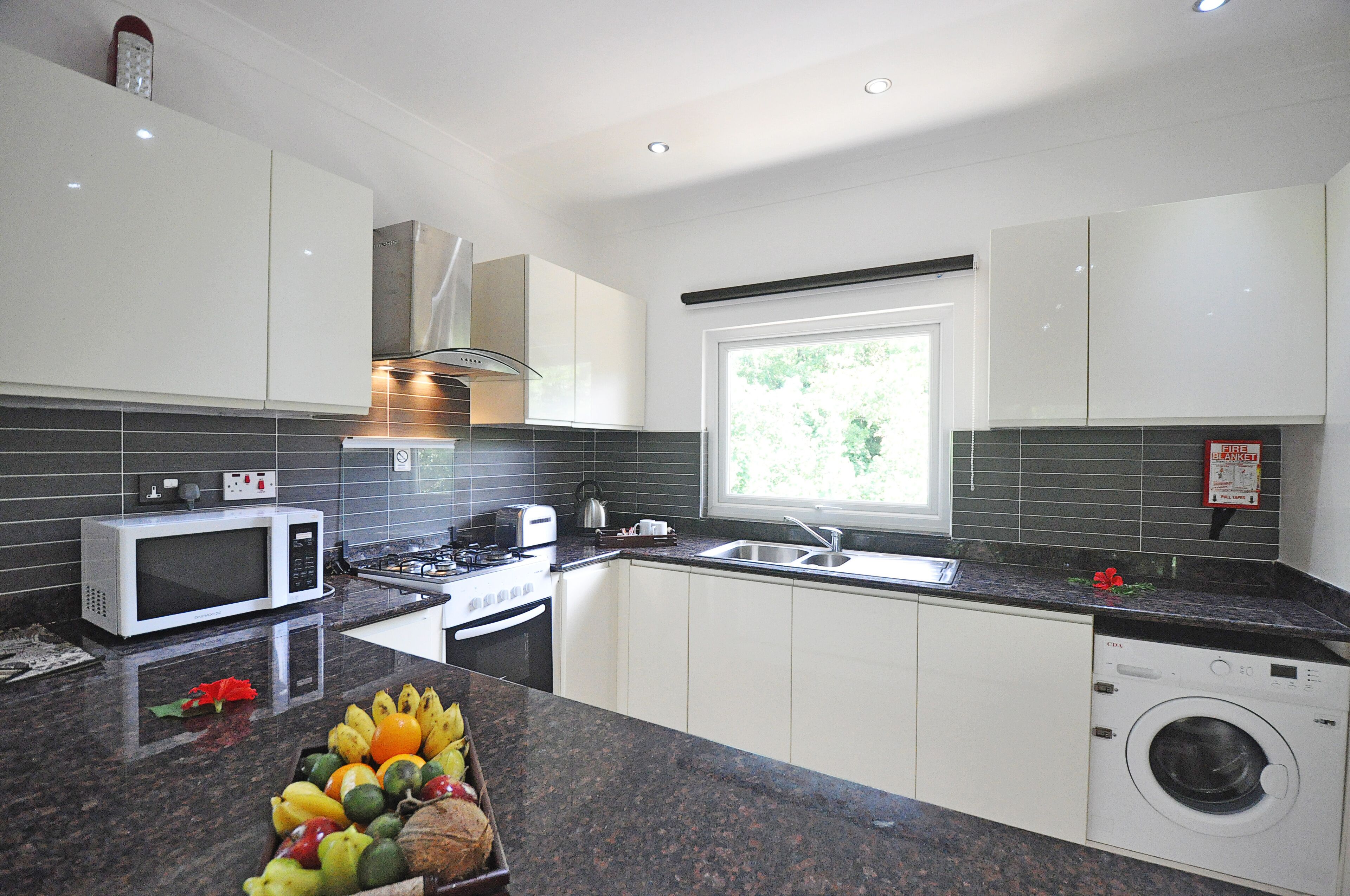 A modern kitchen with white cabinets, a microwave, stove, sink, and a built-in washing machine.