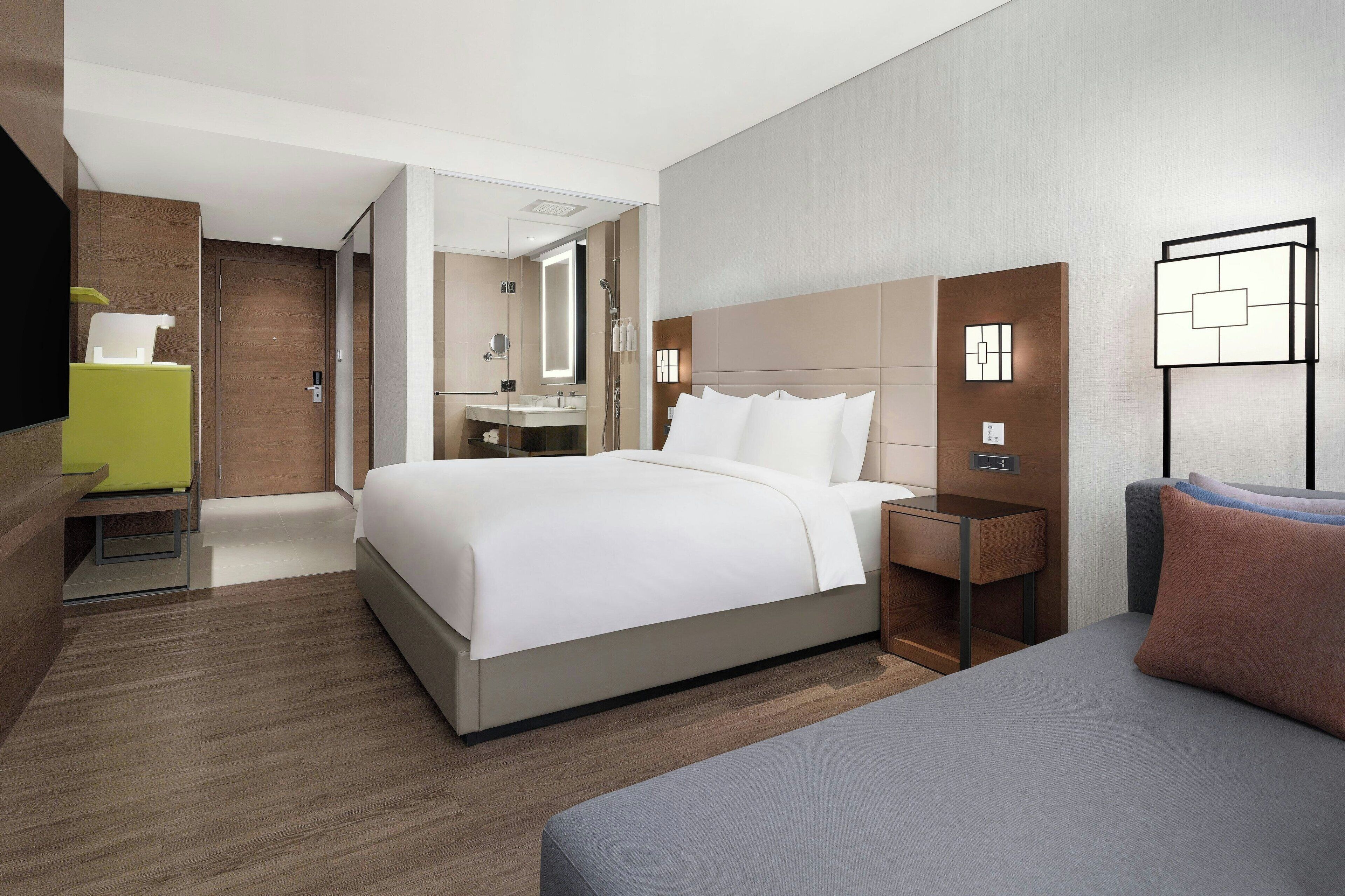 Una habitación de hotel moderna con una cama grande, mesitas de noche, un escritorio, una silla, un espejo y un televisor.
