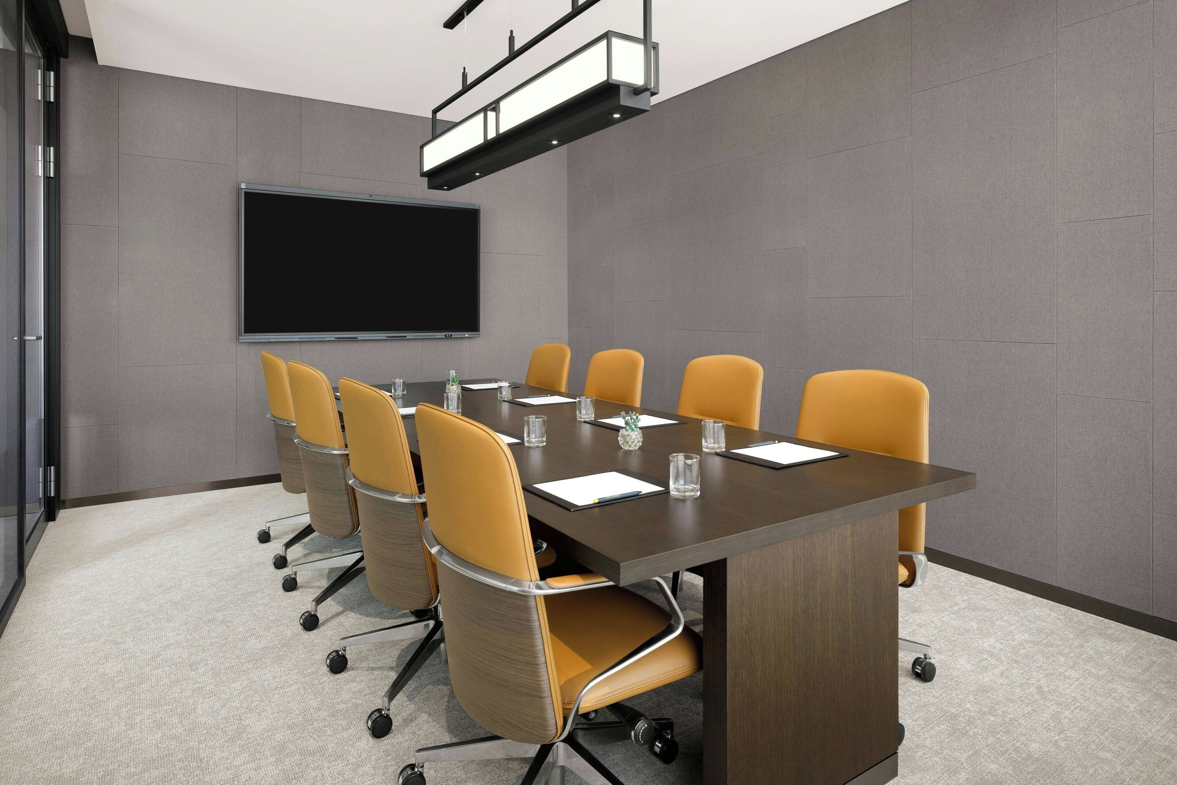 Een vergaderzaal met een grote tafel, zes stoelen, een scherm voor een beamer en een vloerbedekking.