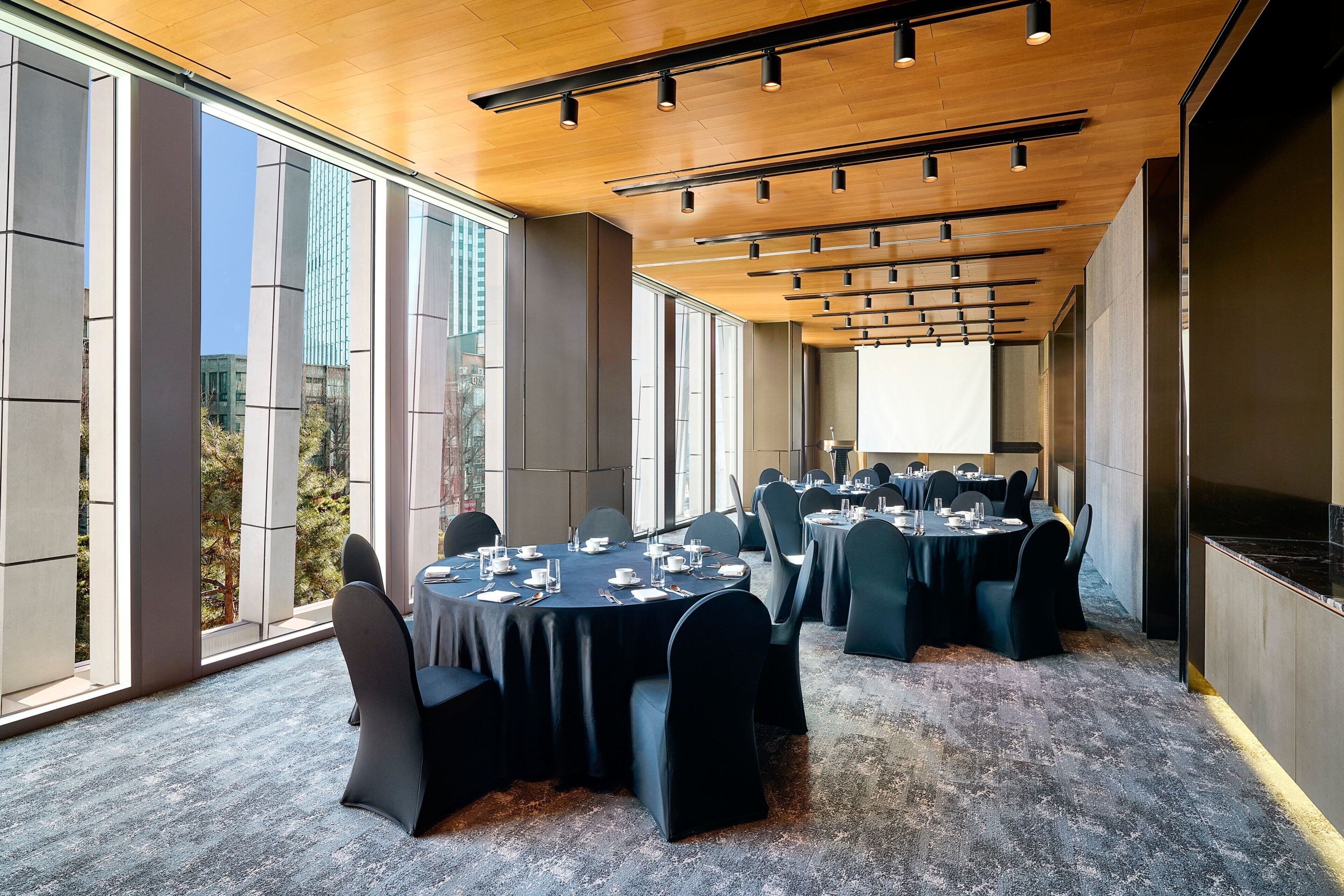 A conference room with round tables, black chairs, and a large window with a city view.