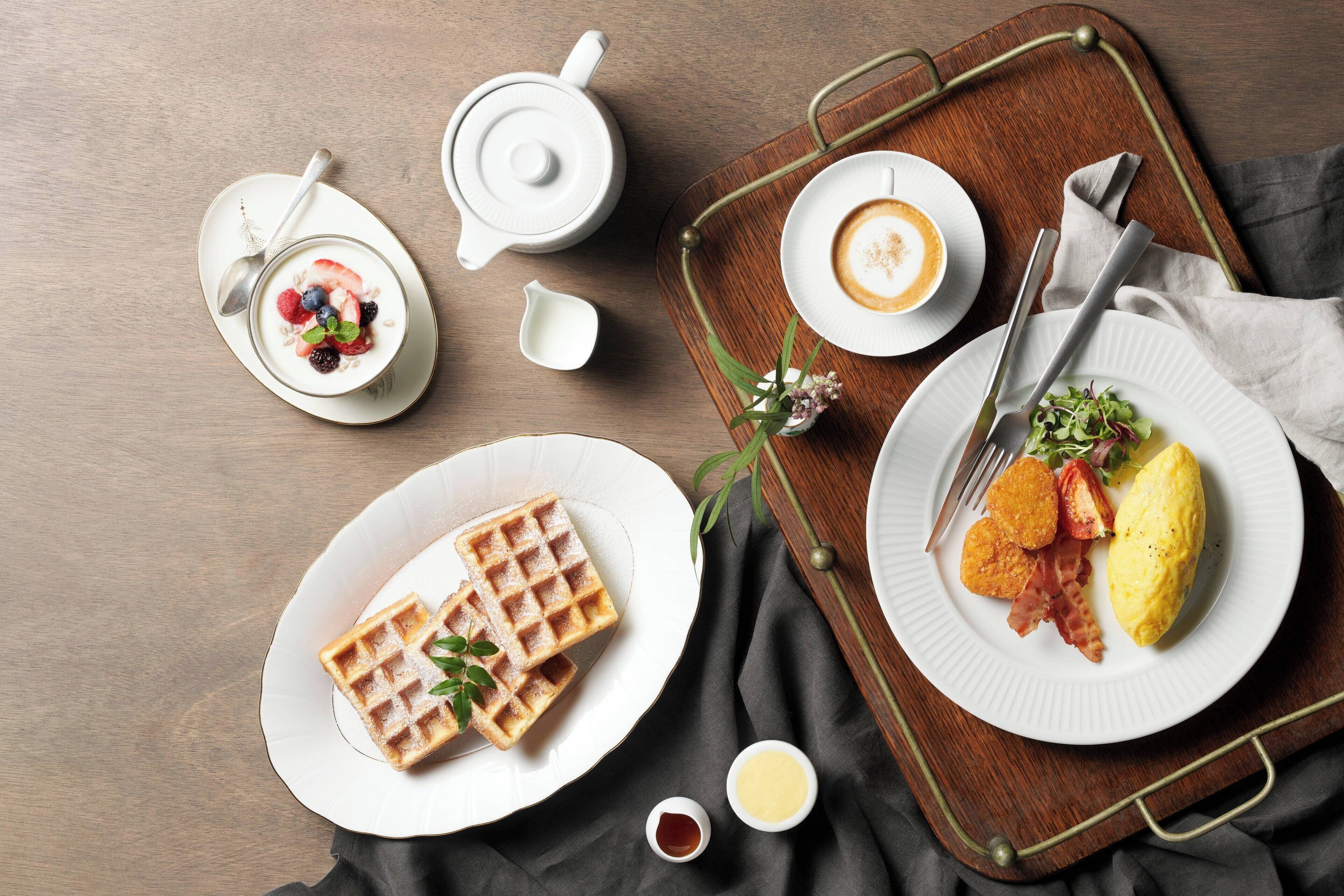 A breakfast tray with waffles, scrambled eggs, bacon, and a cup of coffee.