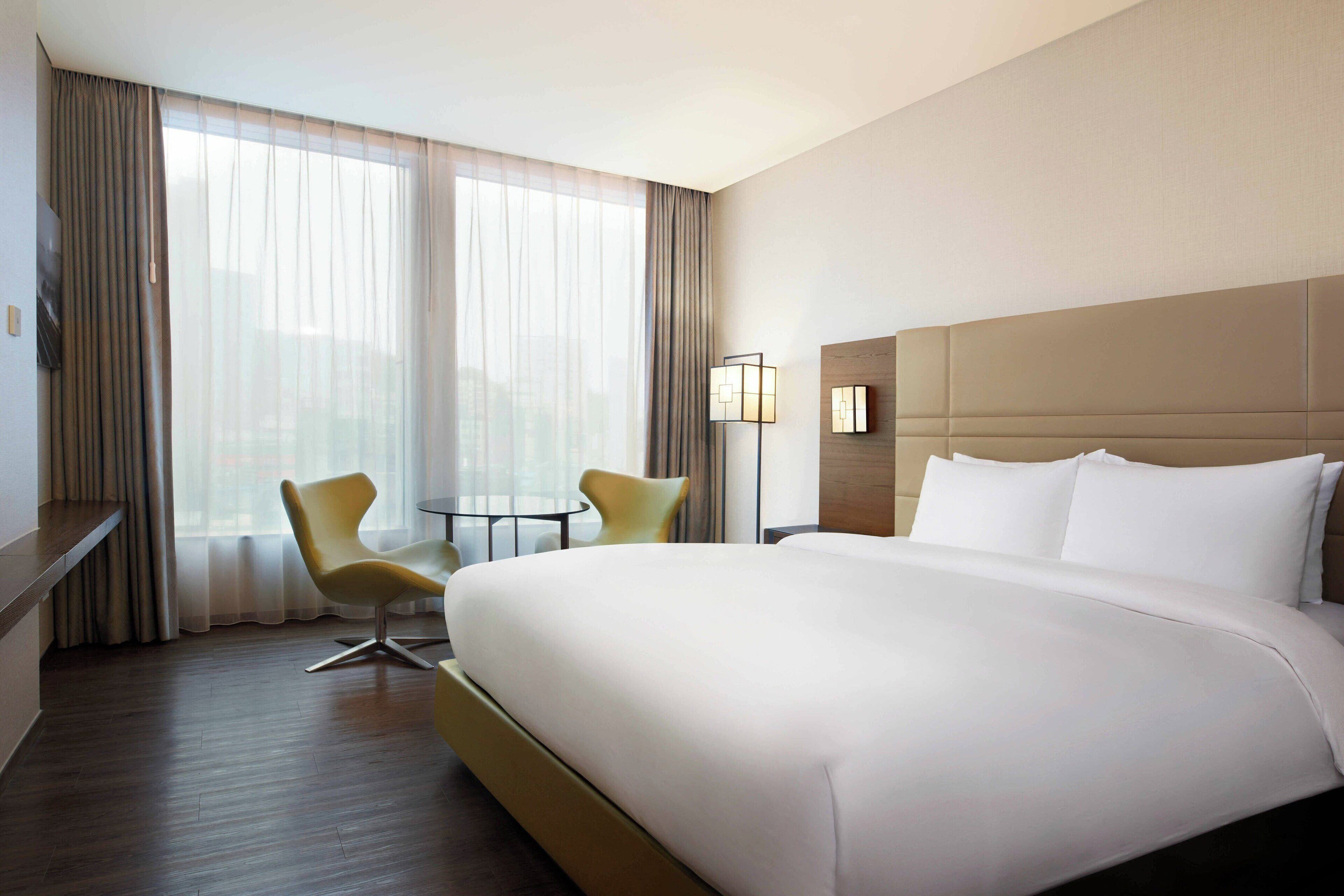 Una habitación de hotel con una cama grande, dos sillas, una mesita y una lámpara.