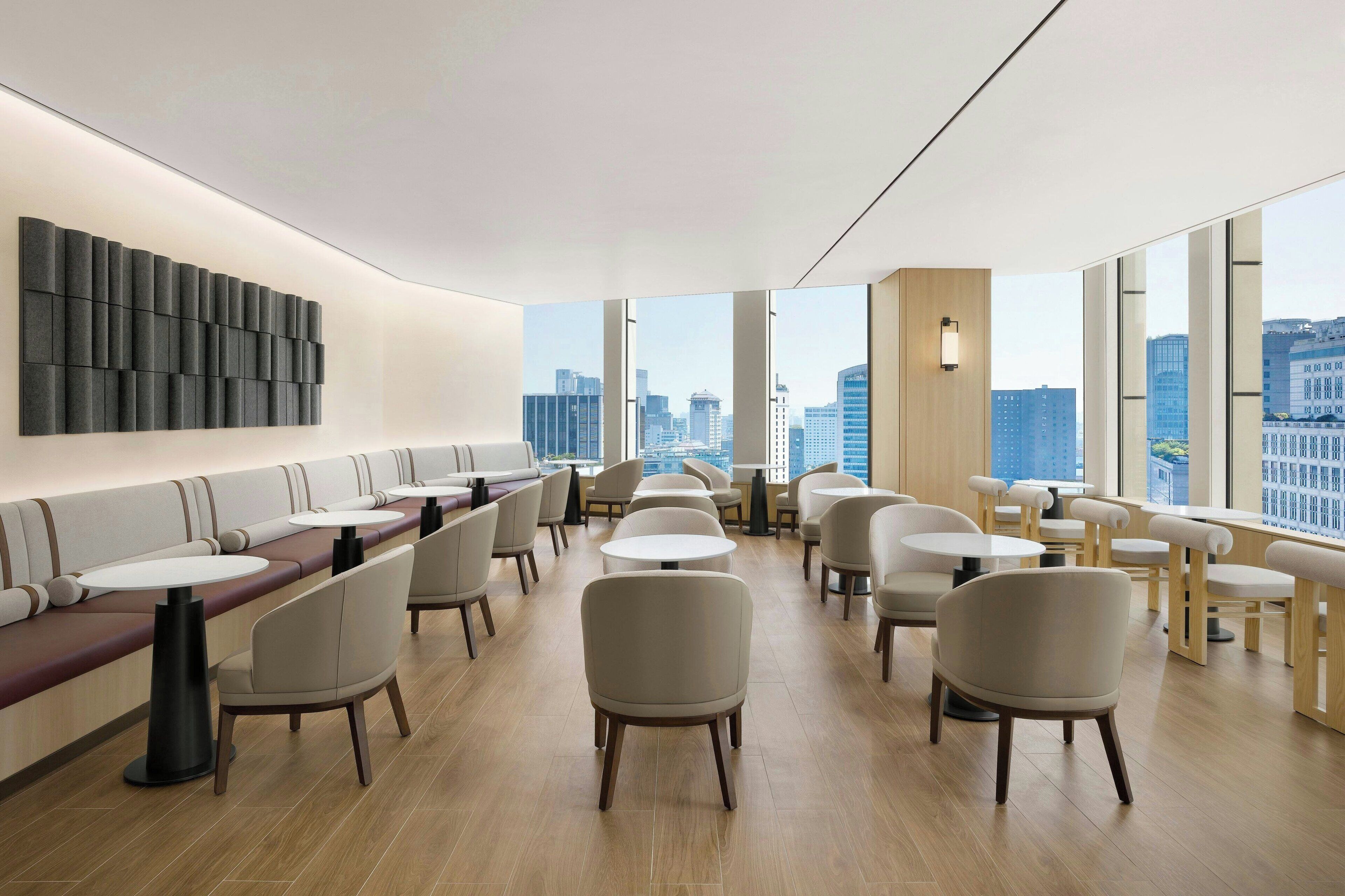 Un restaurante moderno con mesas altas y asientos acolchados, amplias ventanas con vistas a la ciudad.