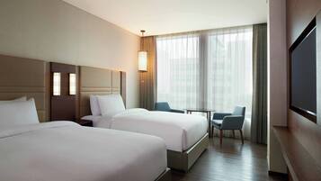 A hotel room with two beds, a desk, a chair, and a TV.