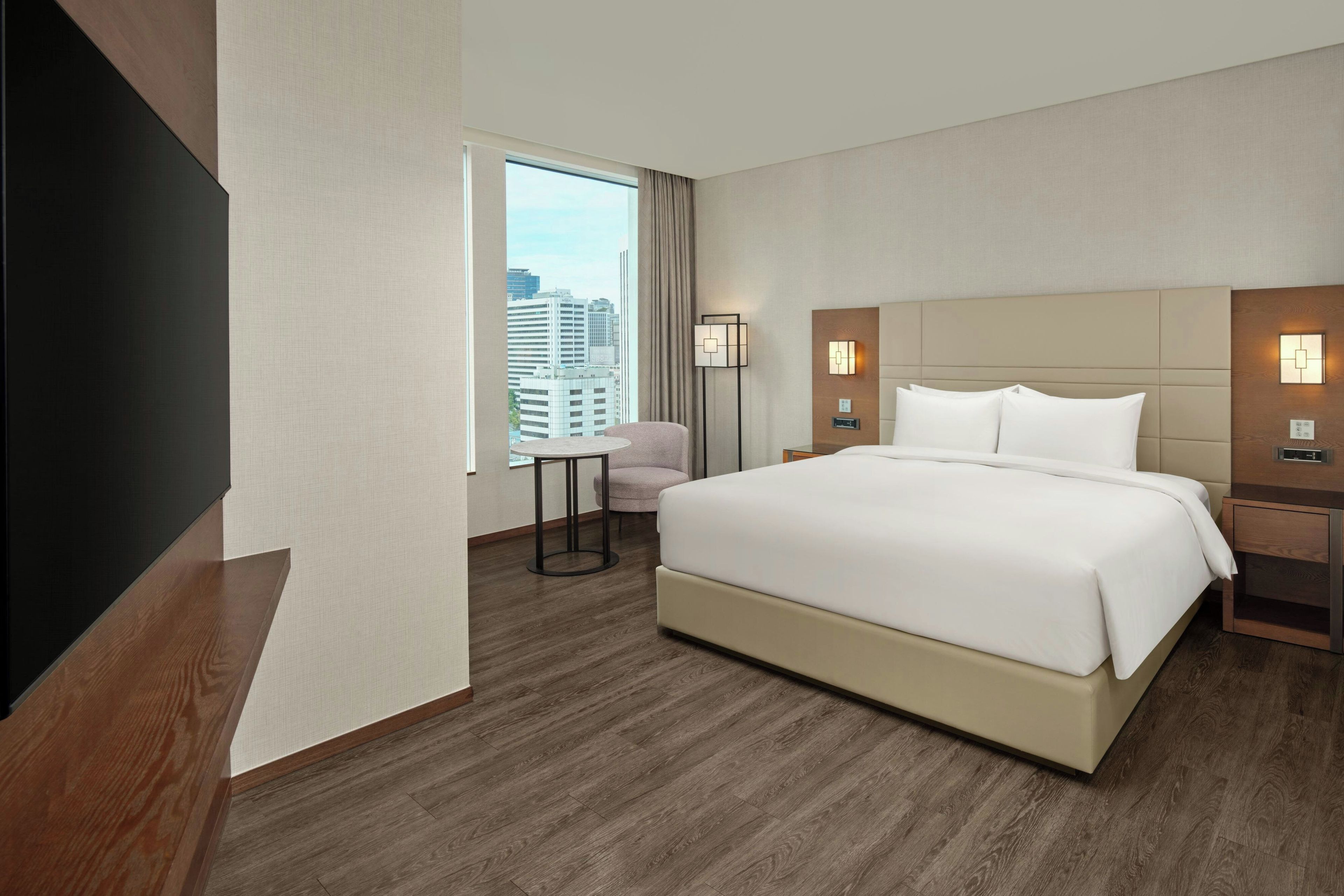 A hotel room with a large bed, a desk, a chair, and a view of the city.