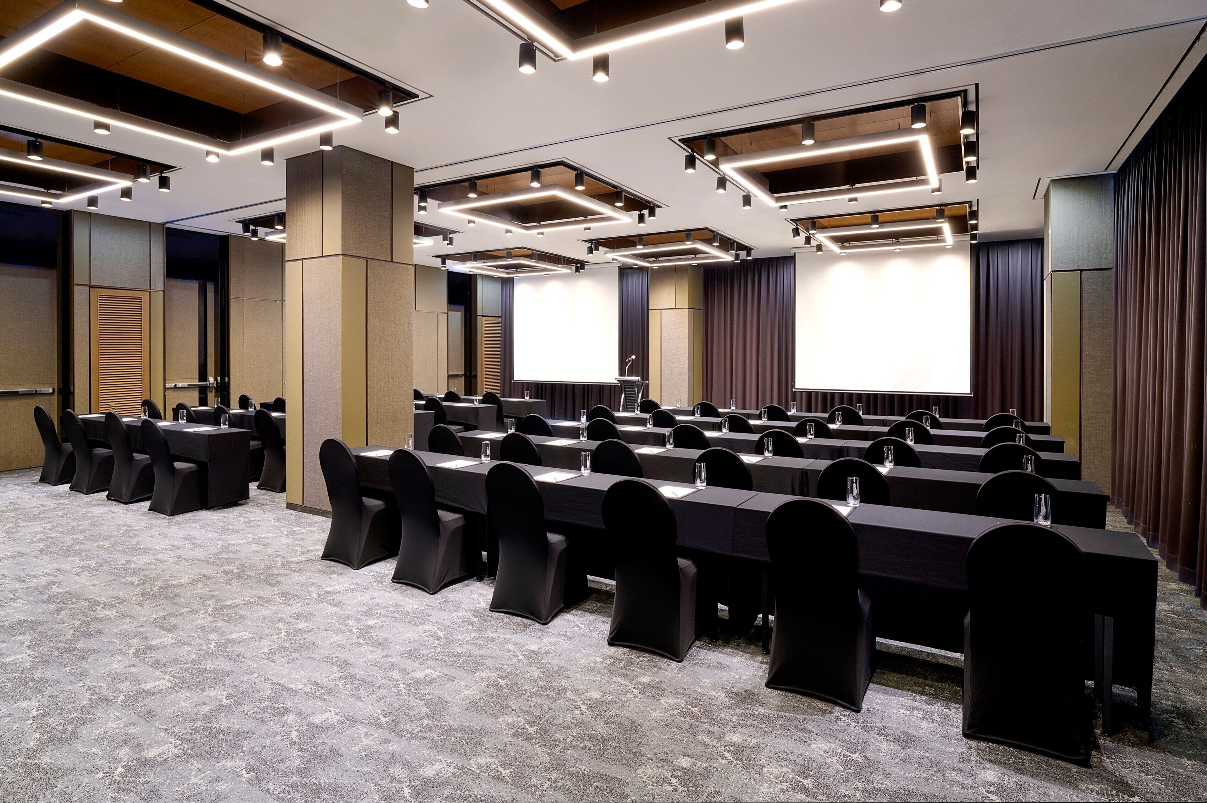 Un salón de conferencias con varias mesas y sillas, equipado con micrófonos y vasos de agua.