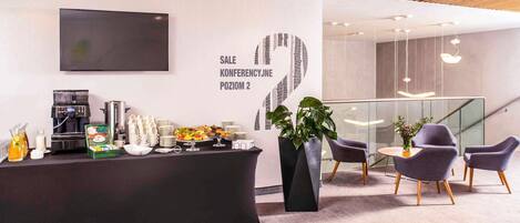 A modern reception area with a coffee station, a large potted plant, and a seating area with chairs and a table.