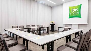 Un salón de conferencias con una larga mesa, sillas, una pantalla de proyector y una mesa con un jarrón de flores.