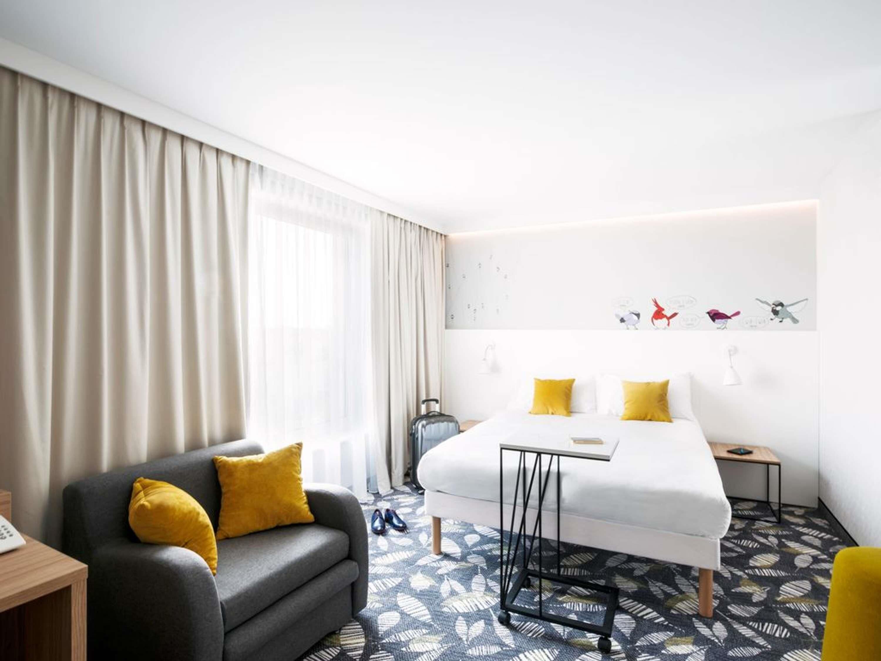 A hotel room with a bed, a sofa, a desk, and a window with curtains.
