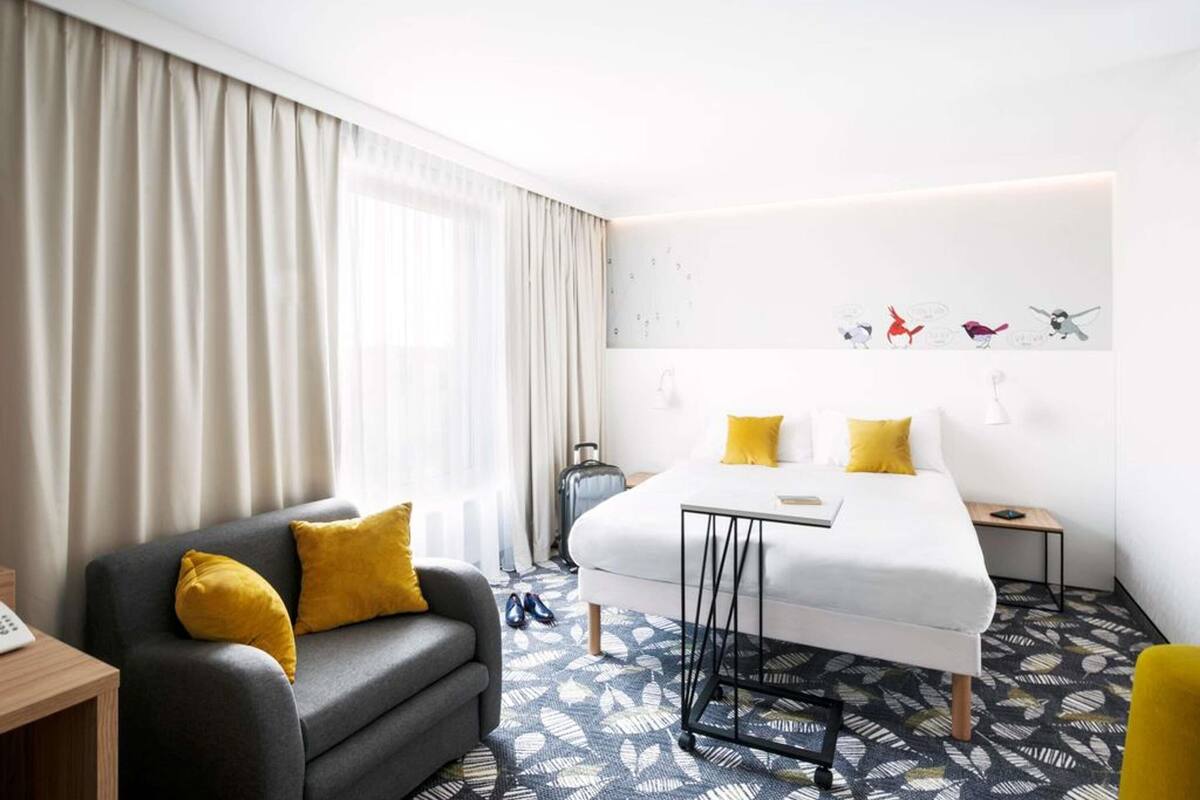 Habitación de hotel con cama, sofá, escritorio y ventana con cortinas.