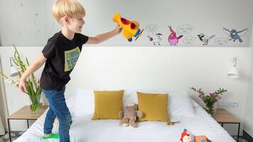 Cozy room for kids, featuring a comfortable bed with a teddy bear and toys, a small table with a vase of flowers, and a fun wall of colorful artwork.