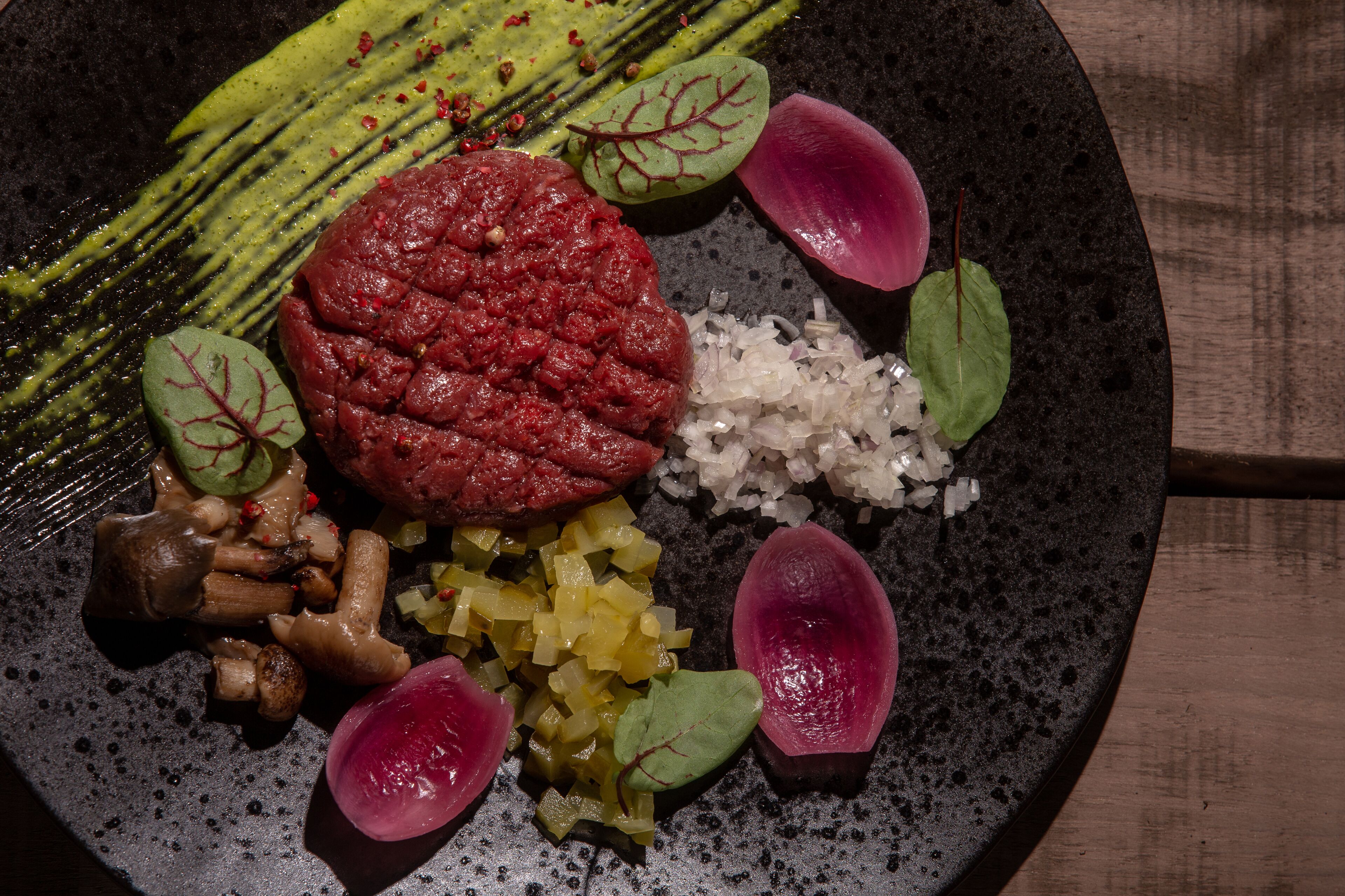 A plate with various food items including a red meat patty, diced vegetables, and garnishes.