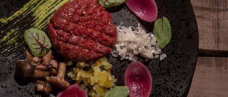 A plate with various food items including a red meat patty, diced vegetables, and garnishes.
