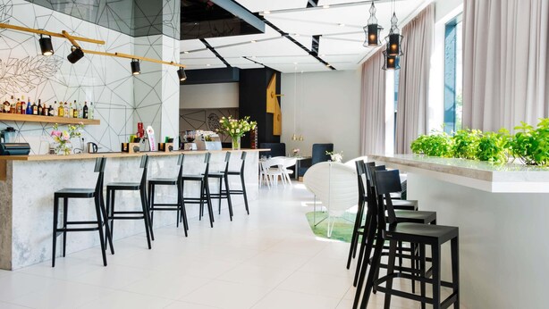 Zona de bar moderna con mostrador, taburetes y un espacio de estar con mesas y sillas.