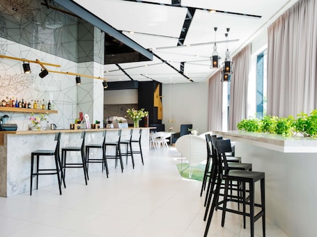 A modern bar area with a counter, bar stools, and a seating area with tables and chairs.. Hotel ibis Styles Bialystok