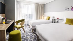 Habitación de hotel con dos camas, un escritorio con una computadora portátil y un teléfono, una silla y una mesita de noche con una lámpara.