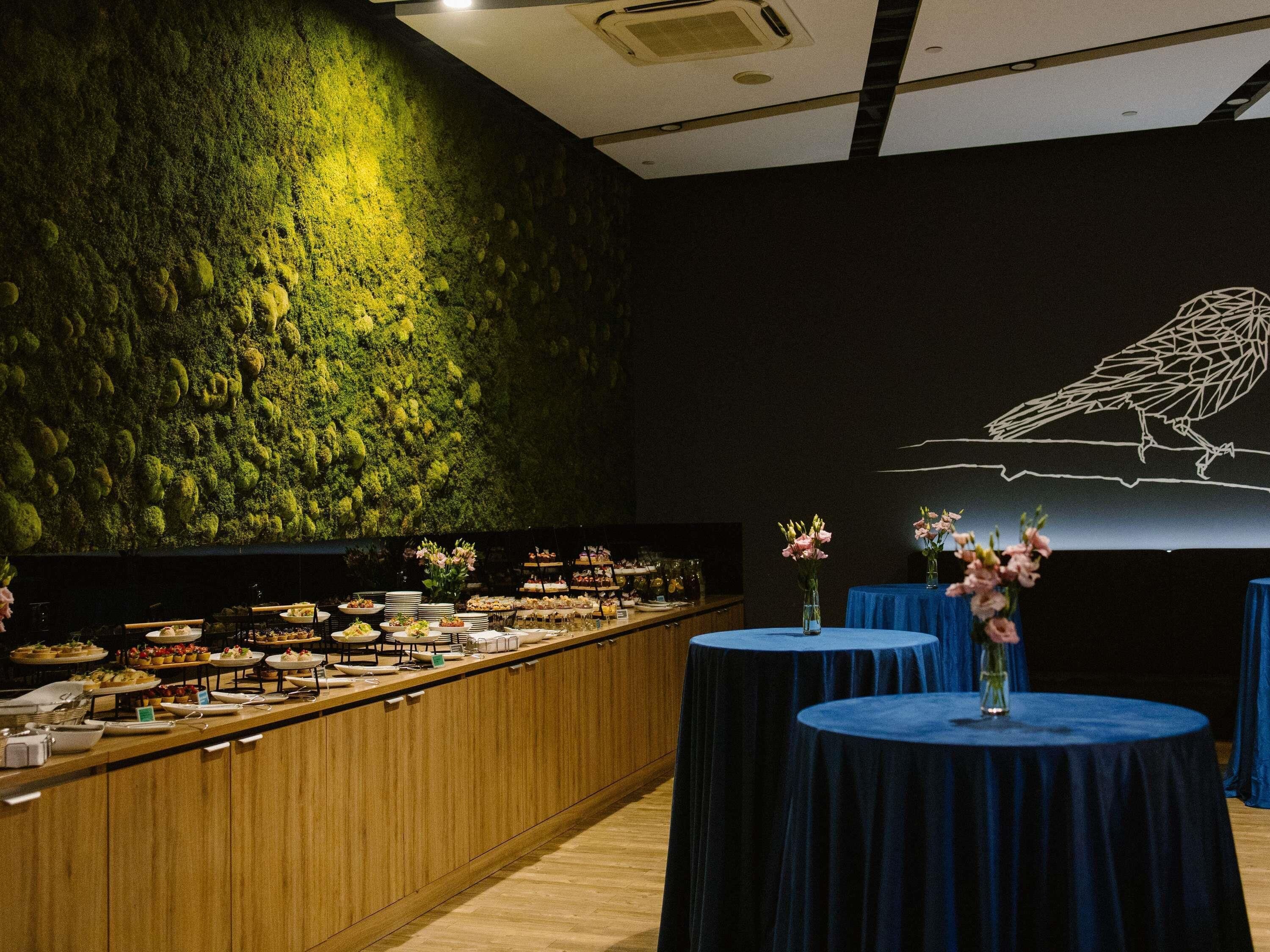 A buffet setup with a variety of dishes, a wall with a moss-like texture, and a bird illustration on the wall.