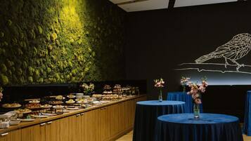 A buffet setup with a variety of dishes, a wall with a moss-like texture, and a bird illustration on the wall.
