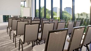 Una sala de conferencias con filas de sillas, ventanas amplias y una pizarra.