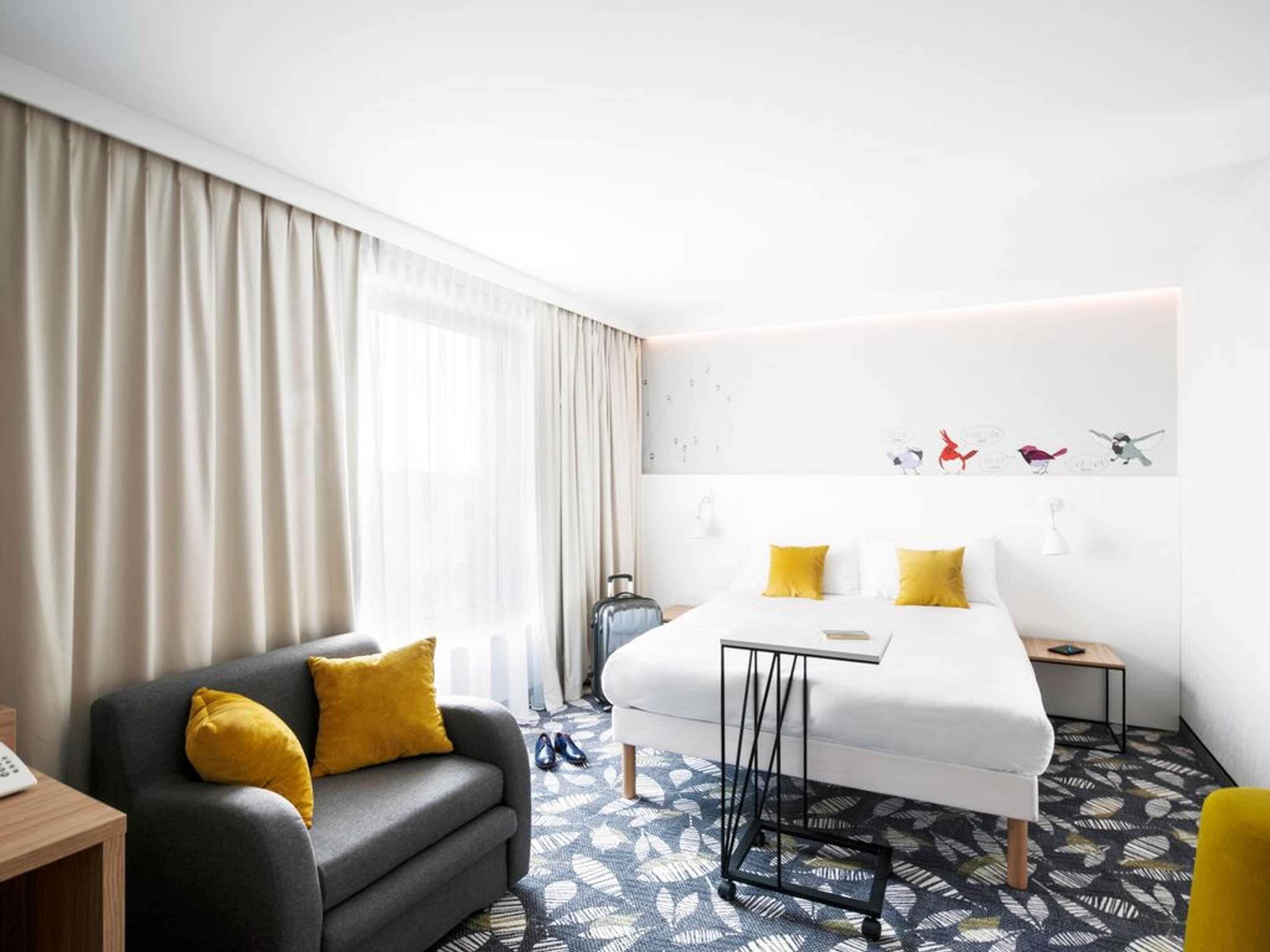 Habitación de hotel con cama, sofá, escritorio y ventana con cortinas.