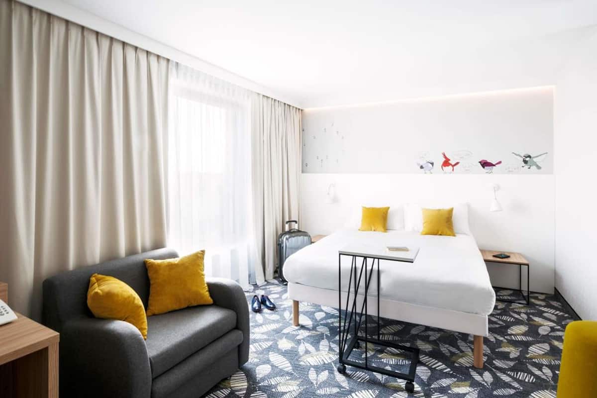 A hotel room with a bed, a sofa, a desk, and a window with curtains.