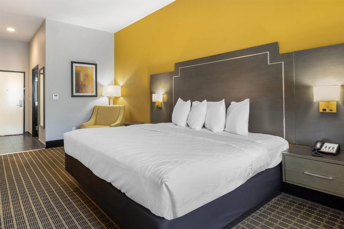 A hotel room with a large bed, two bedside lamps, a nightstand with a phone, and a door leading to another room.