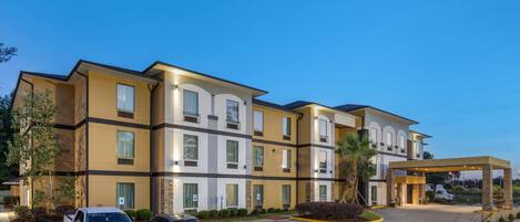 A multi-story hotel with a modern design, featuring a parking lot with several vehicles.