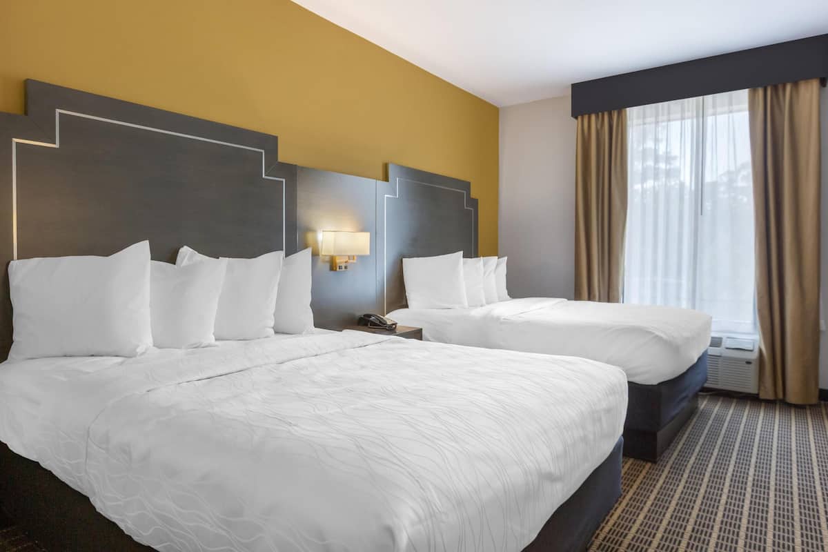 A hotel room with two beds, a headboard with a geometric design, a bedside lamp, and a window with curtains.