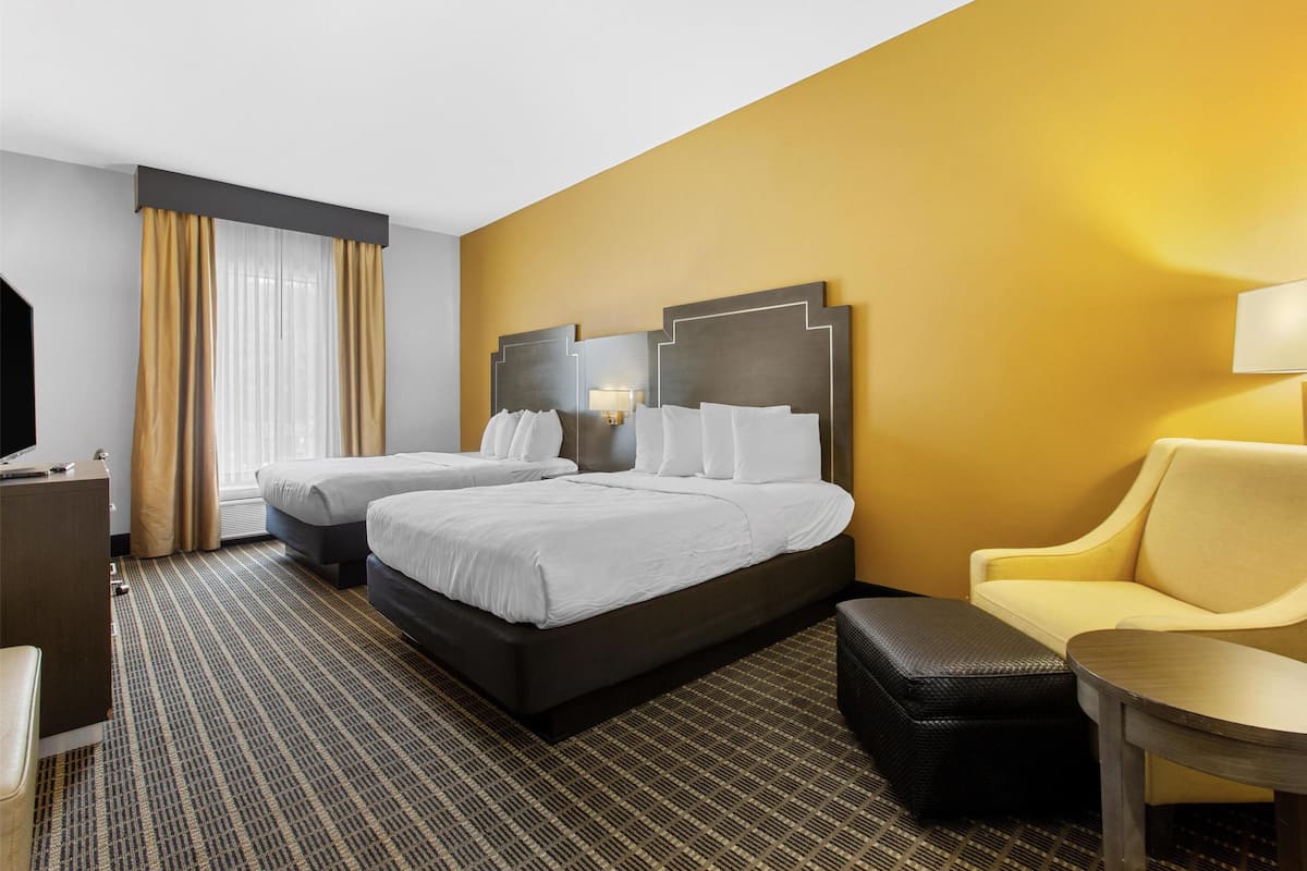 A hotel room with two beds, a sofa, a desk, and a lamp.