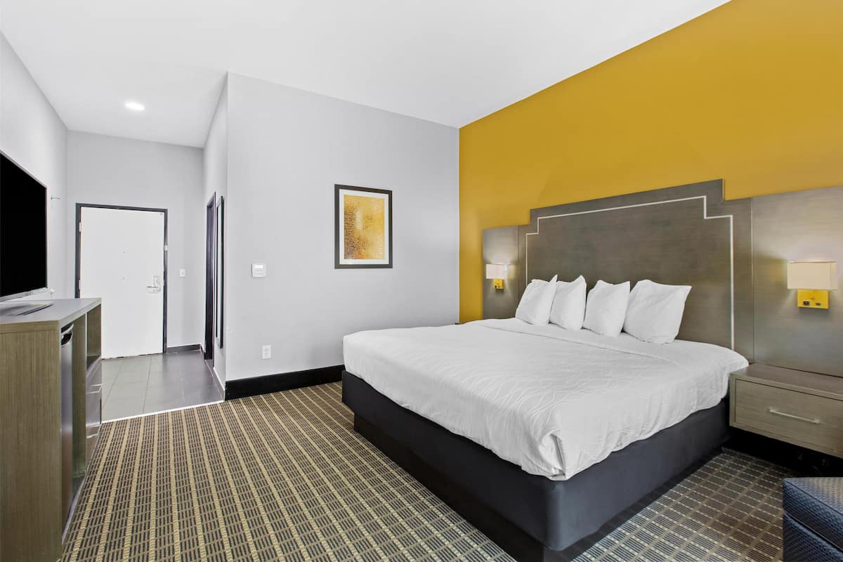 A hotel room with a large bed, a bedside table, a nightstand, a desk, and a chair.