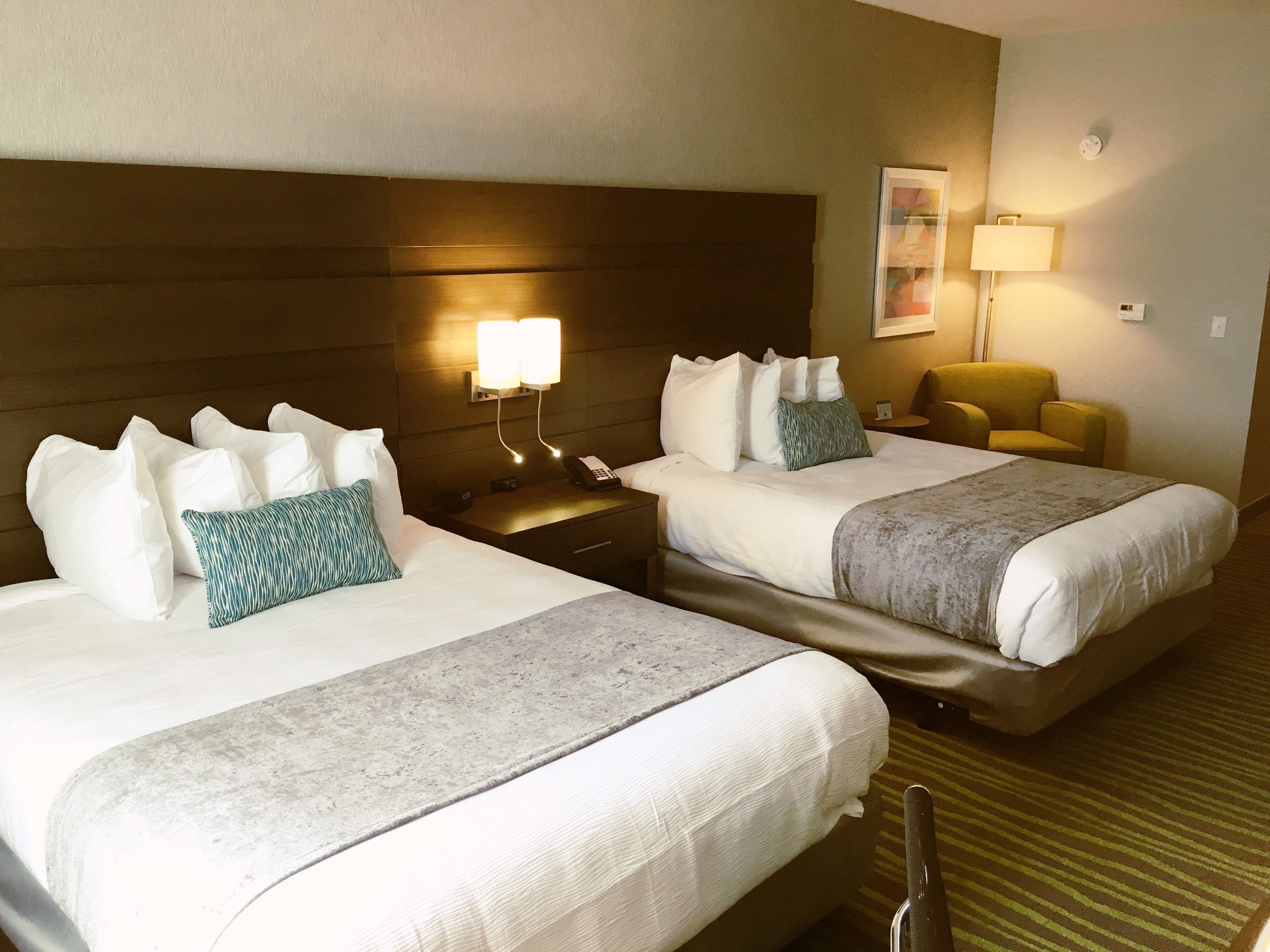 A hotel room with two beds, a nightstand with a phone, a lamp, and a chair.