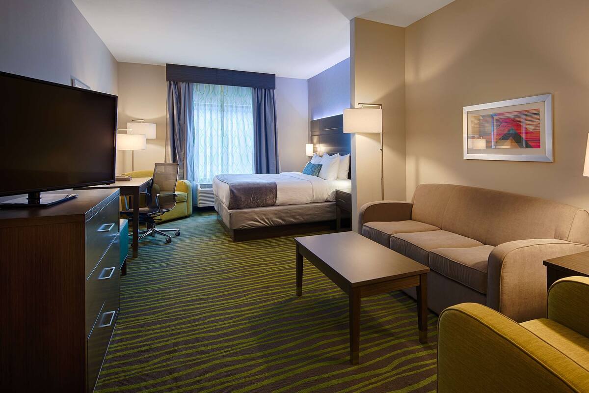 A hotel room with a bed, a sofa, a TV, a desk, and a chair.