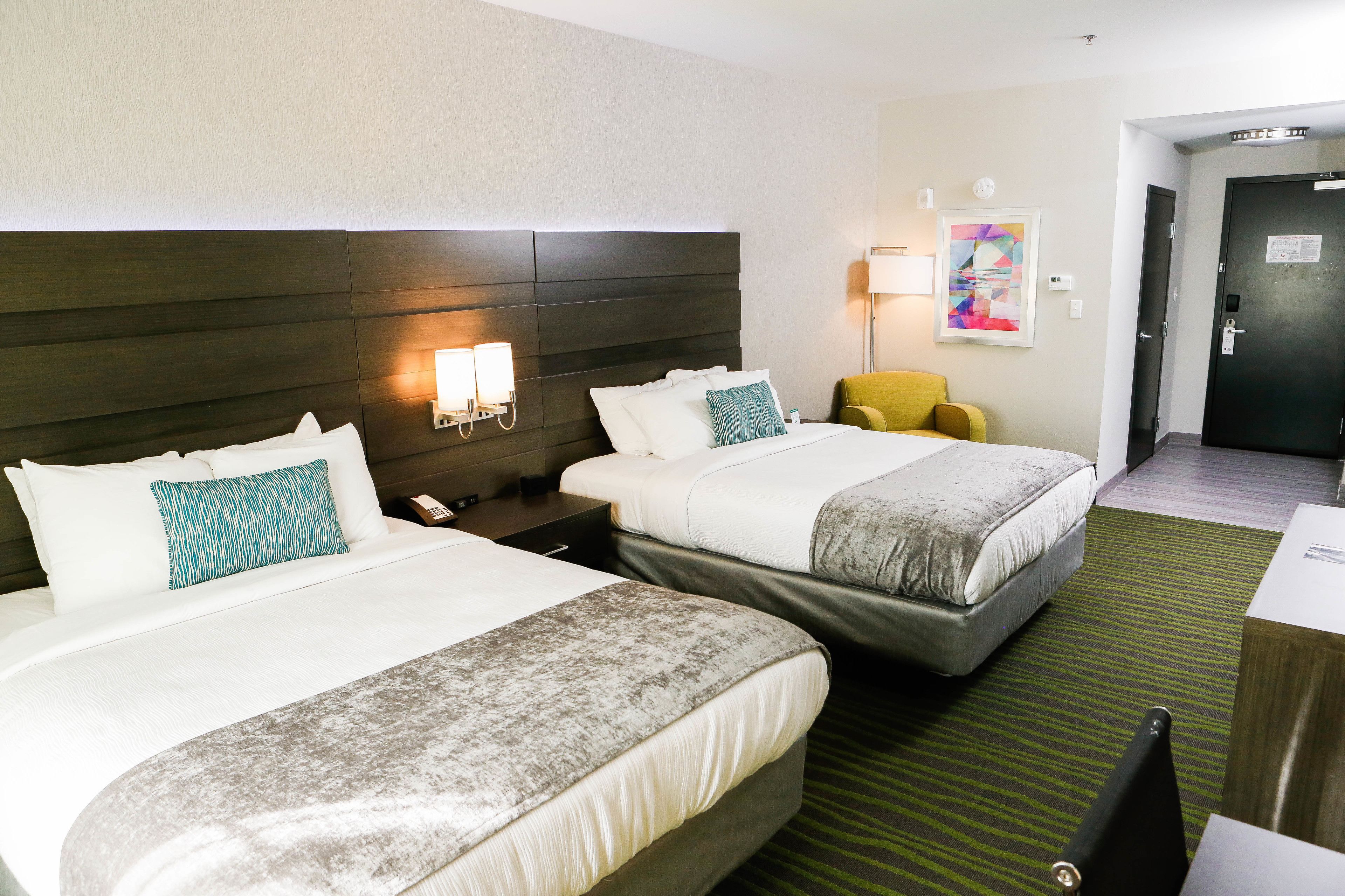 Habitación de hotel con dos camas, una mesita de noche, una lámpara, una silla y una puerta.