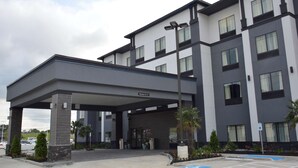 Une entrée d’hôtel moderne, dotée d’un espace abrité, d’un parking et d’un panneau indiquant l’entrée réservée aux clients.