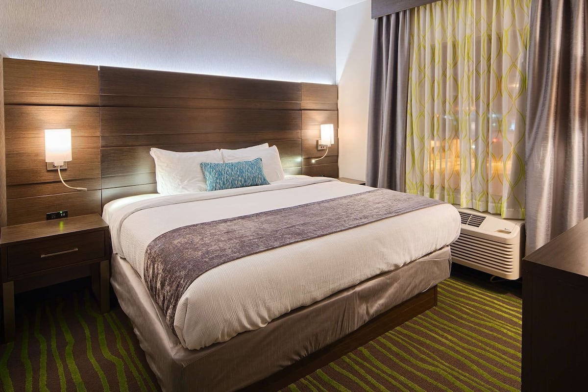 A hotel room with a large bed, bedside lamps, a TV, and a window with curtains.