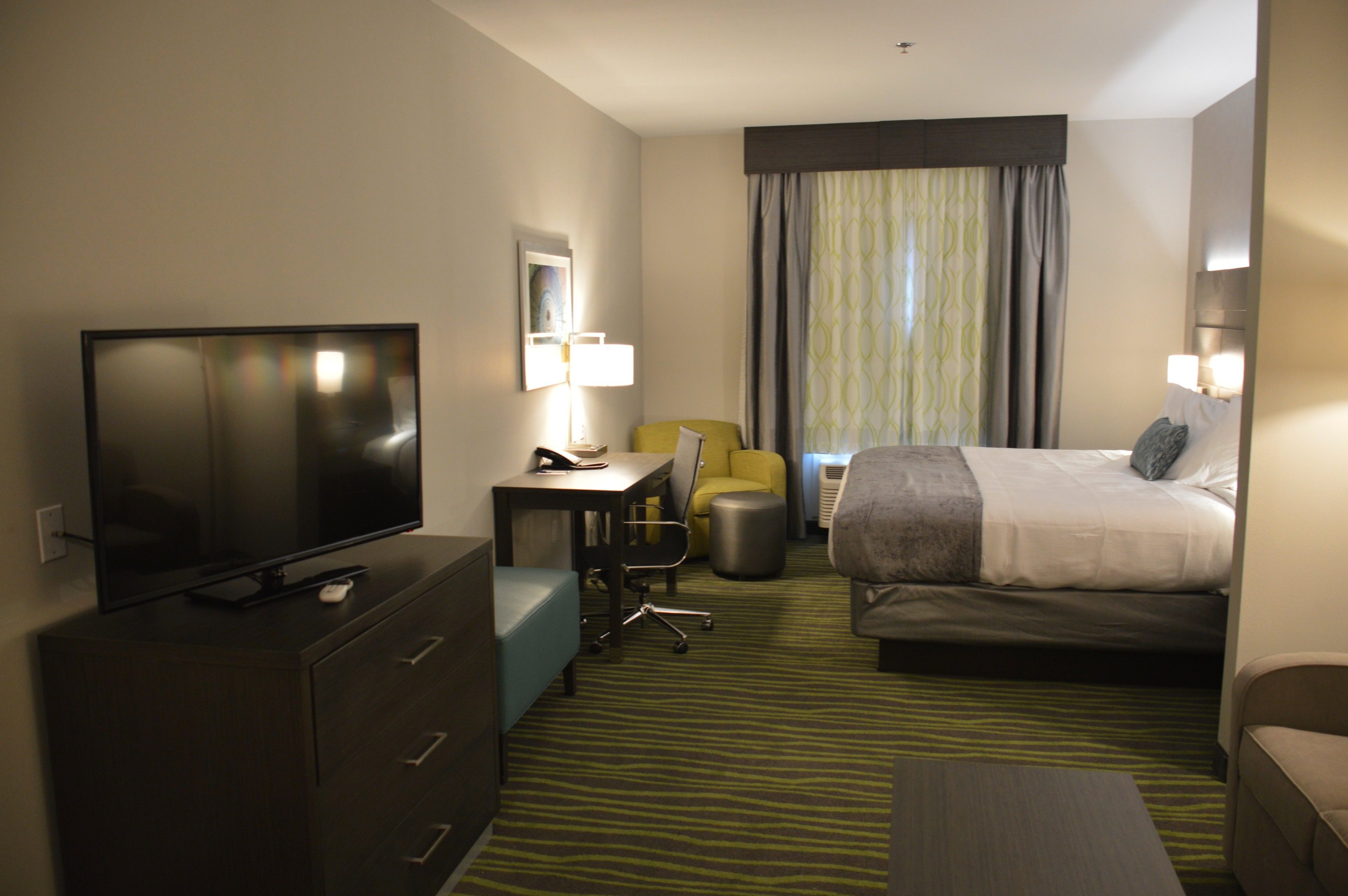 A hotel room with a bed, a desk with a computer, a television, a chair, and a lamp.