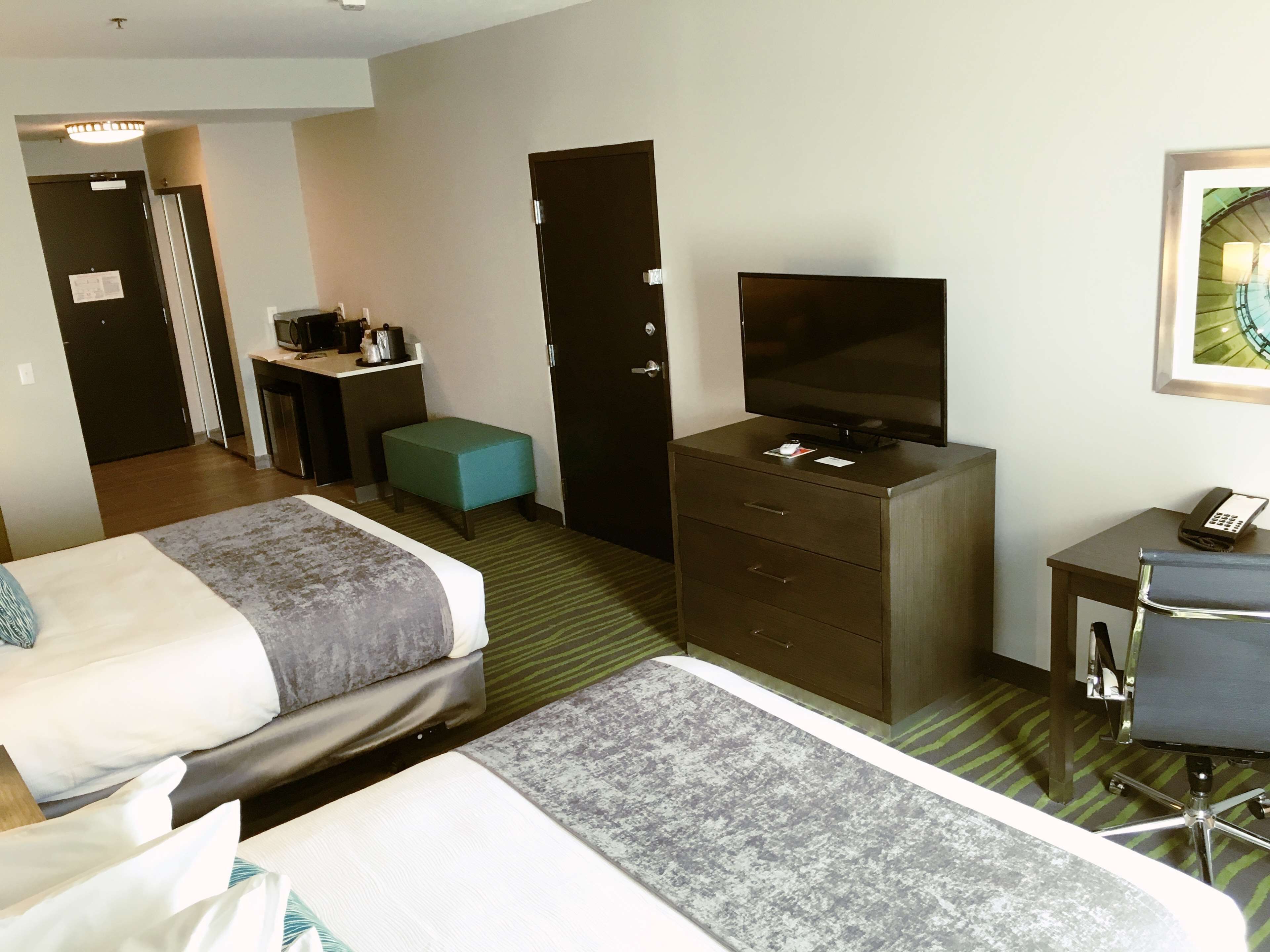 A hotel room with two beds, a desk with a computer, a television, a small table with a phone, and a chair.